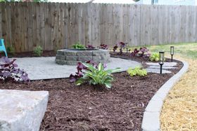 Curved backyard garden bed with mulch, hostas, stone edging, and a wooden fence.