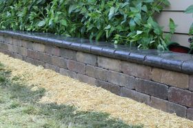 Raised brick garden wall with gray capstone beside mulch and green shrubs