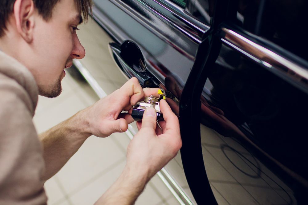 Gloved Hands Using a Tool to Open a Car Door Handle on A Black Vehicle — Terrace Locksmiths in Raymond Terrace, NSW