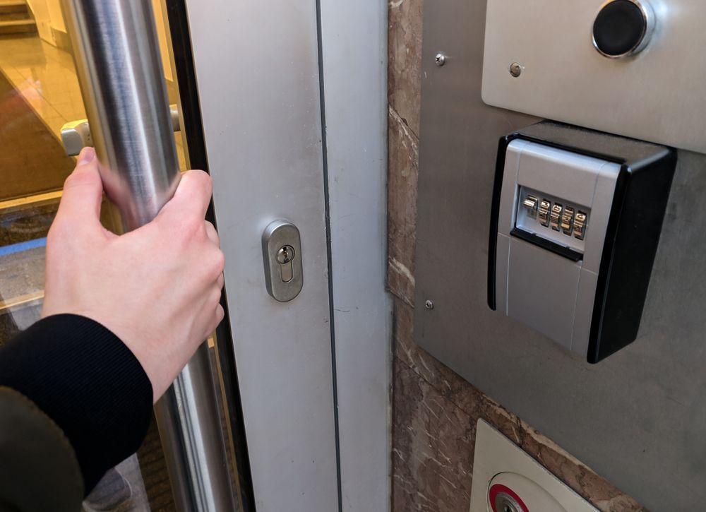 Hand Holding a Metal Pole Beside a Building Entrance Keypad and Door Lock — Terrace Locksmiths in Charlestown, NSW