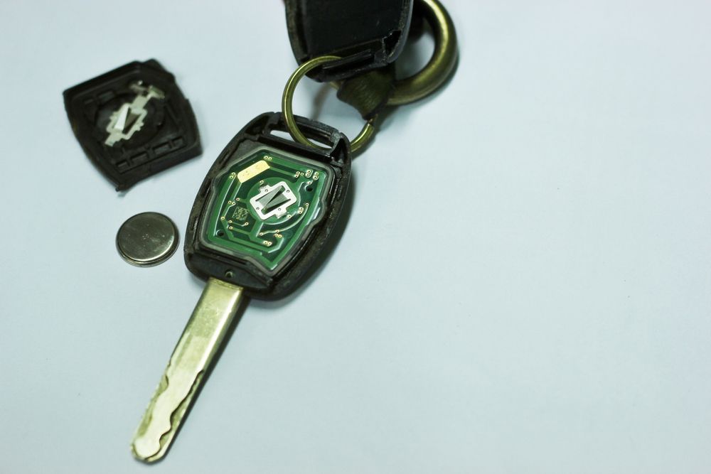 Green Key Fob with Metal Key, a Small Coin, and A Black Case on A White Surface — Terrace Locksmiths in Nelson Bay, NSW
