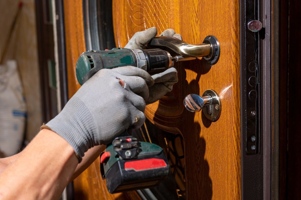 Gloved Hands Using a Power Drill to Install a Lock on A Wooden Door — Terrace Locksmiths in Nelson Bay, NSW