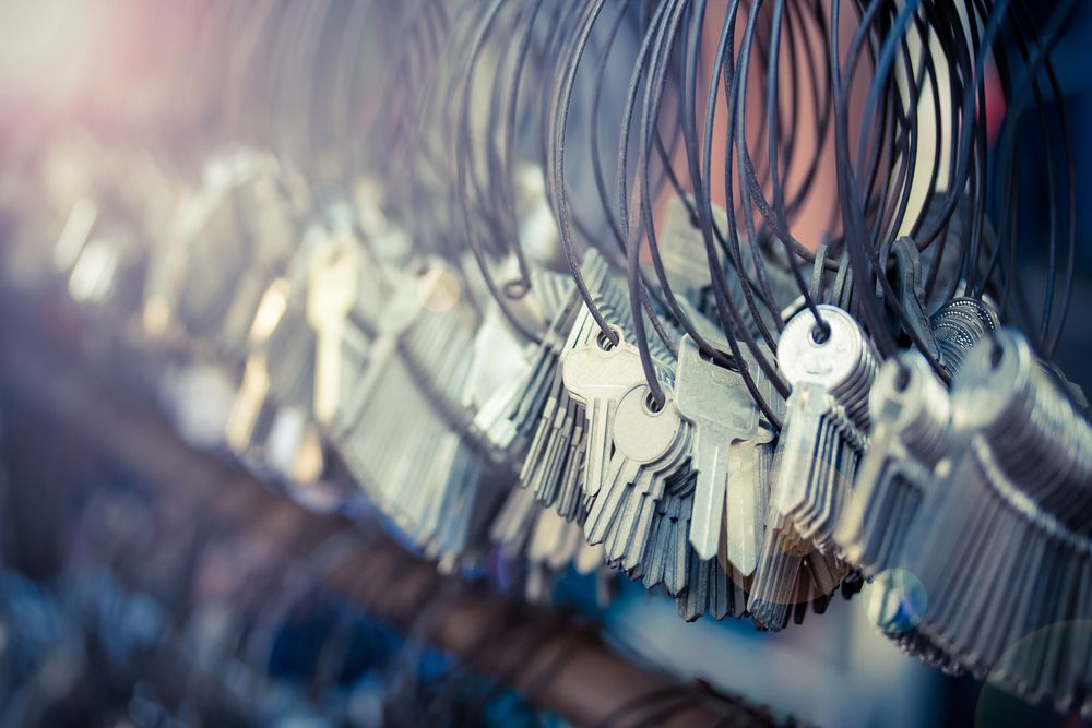 Close-up of rows of keys hanging on hooks, with a soft blue and pink blurred background — Terrace Locksmiths in Raymond Terrace, NSW