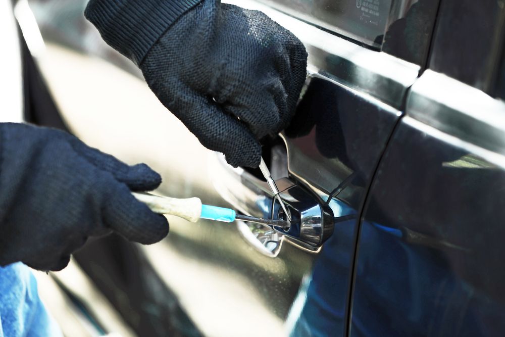 Gloved Hands Use a Tool to Unlock a Car Door Handle on A Dark Blue Vehicle — Terrace Locksmiths in Lake Macquarie, NSW