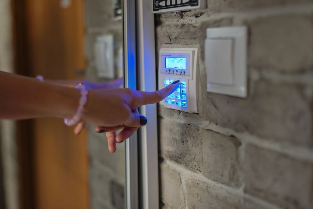 Hand pressing a blue-lit security keypad mounted on a brick wall — Terrace Locksmiths in Raymond Terrace, NSW