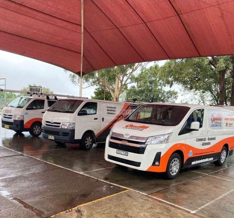 Three white and orange service vans parked under a red canopy on a wet concrete lot— Terrace Locksmiths in Raymond Terrace, NSW