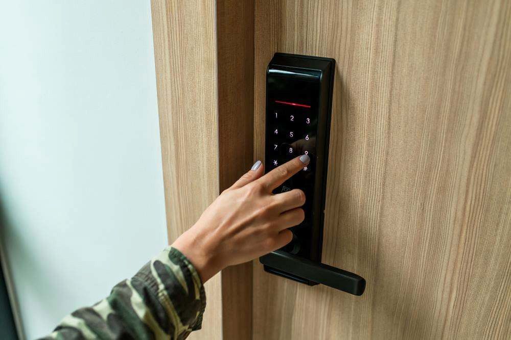 Hand Using a Black Electronic Door Lock on a Wooden Door — Terrace Locksmiths in Raymond Terrace, NSW