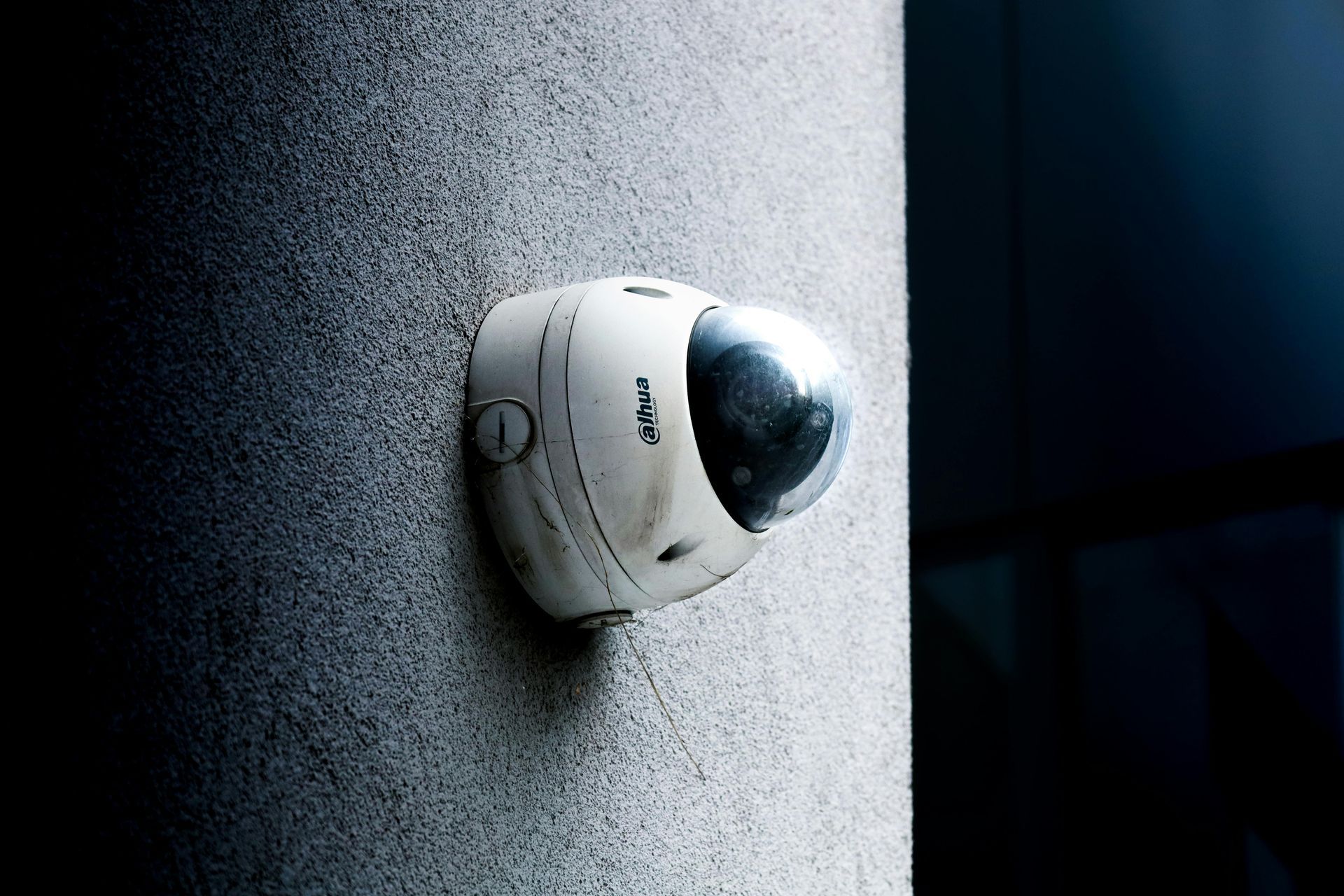 White Security Camera Mounted on A Gray Wall, Angled Toward a Dark Area — Terrace Locksmiths in Raymond Terrace, NSW