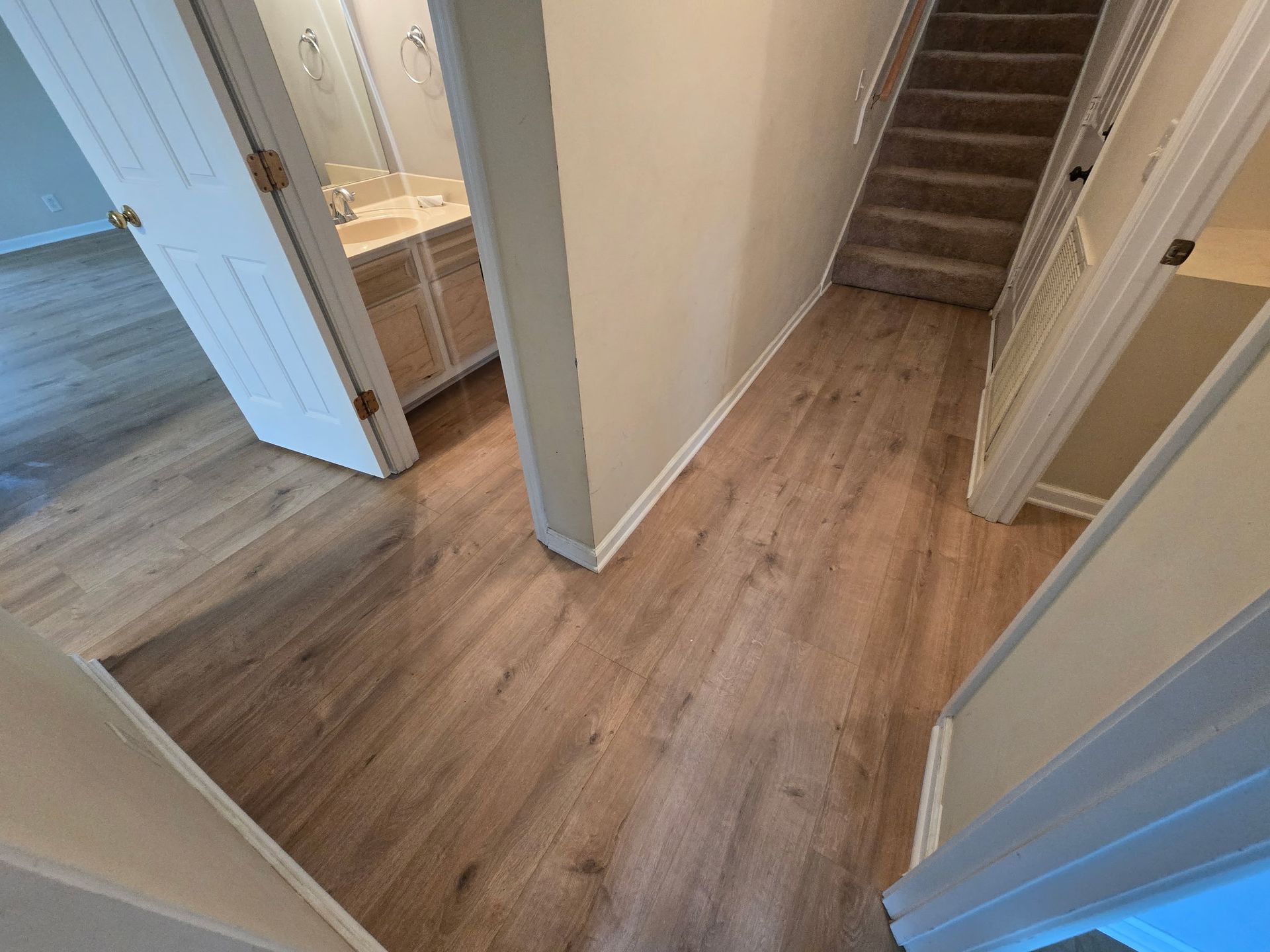 A hallway with hardwood floors leading to a bathroom and stairs.