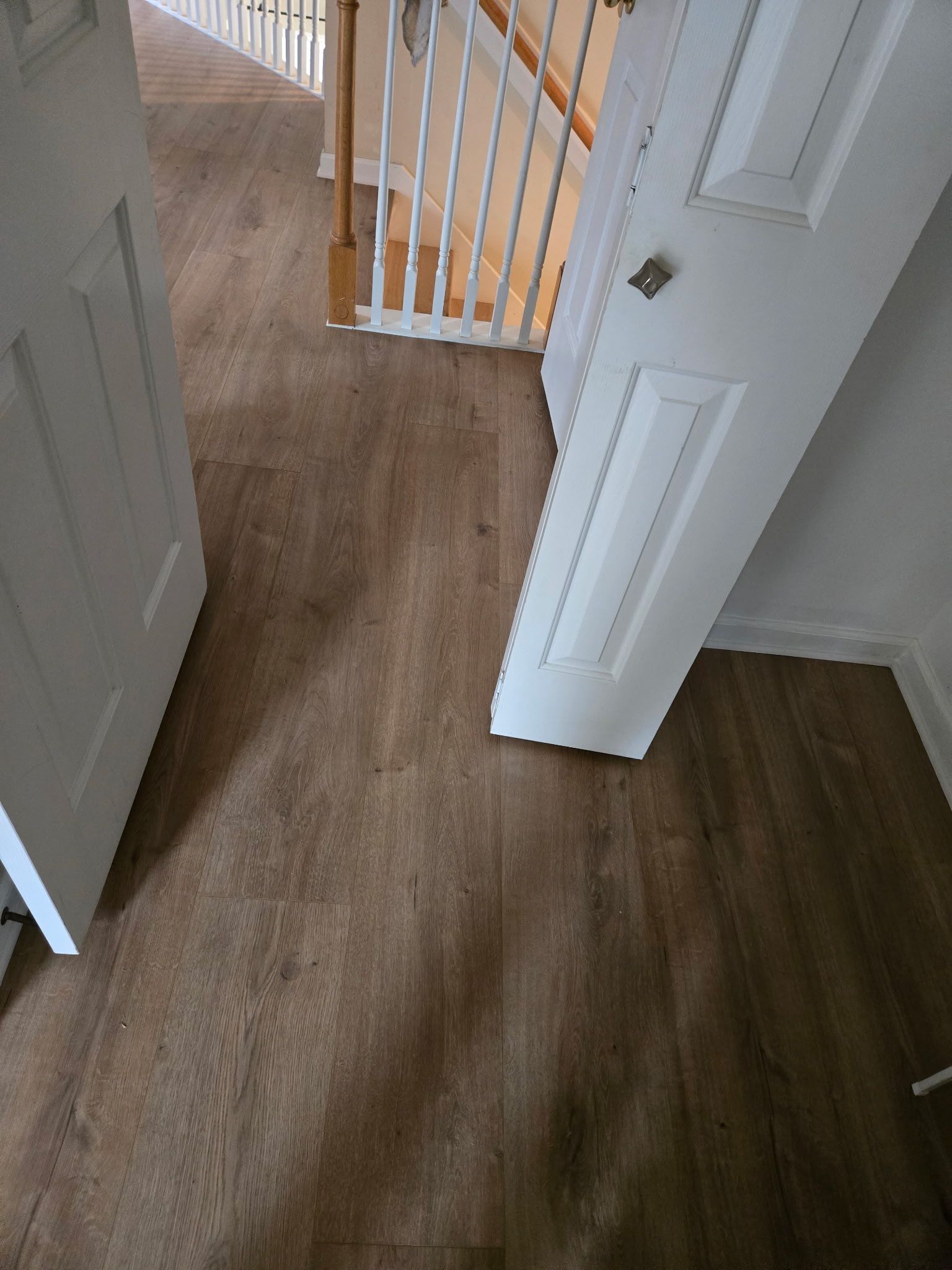 A wooden floor with a white door and stairs in the background.