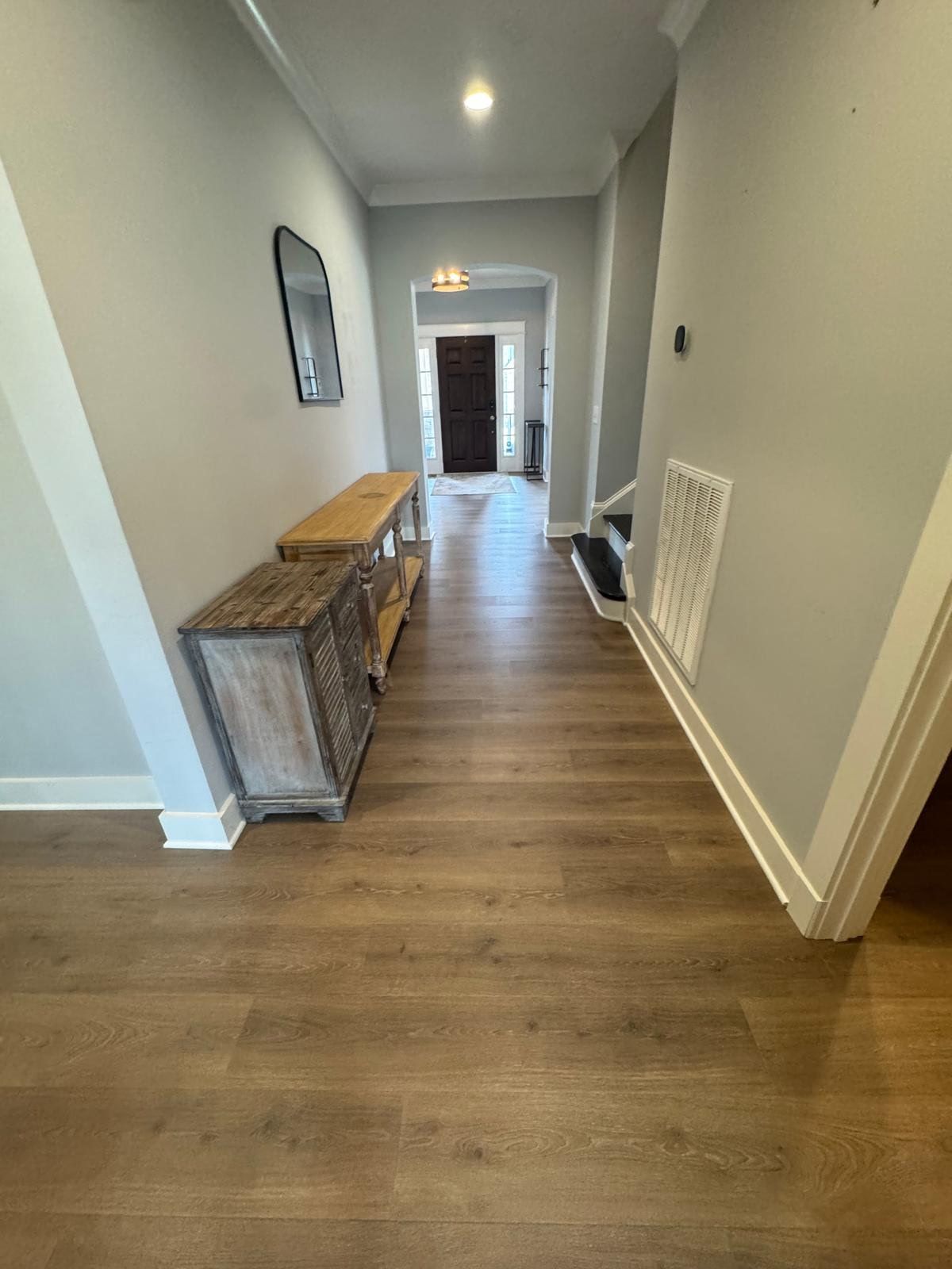 A hallway with hardwood floors and a mirror on the wall.