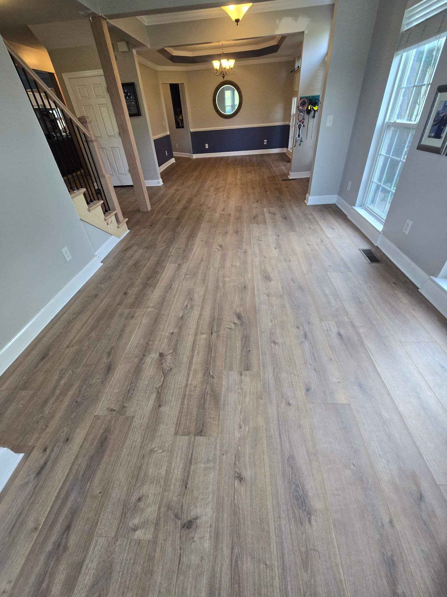 Wood-look flooring in a home's entrance and into the dining area with an oval mirror.