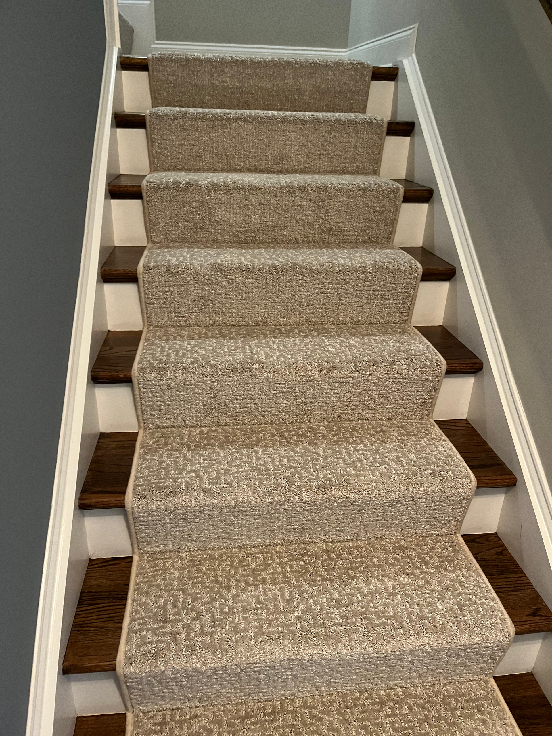 Staircase with beige carpet on treads and wood steps, white risers, and white trim, going upwards.