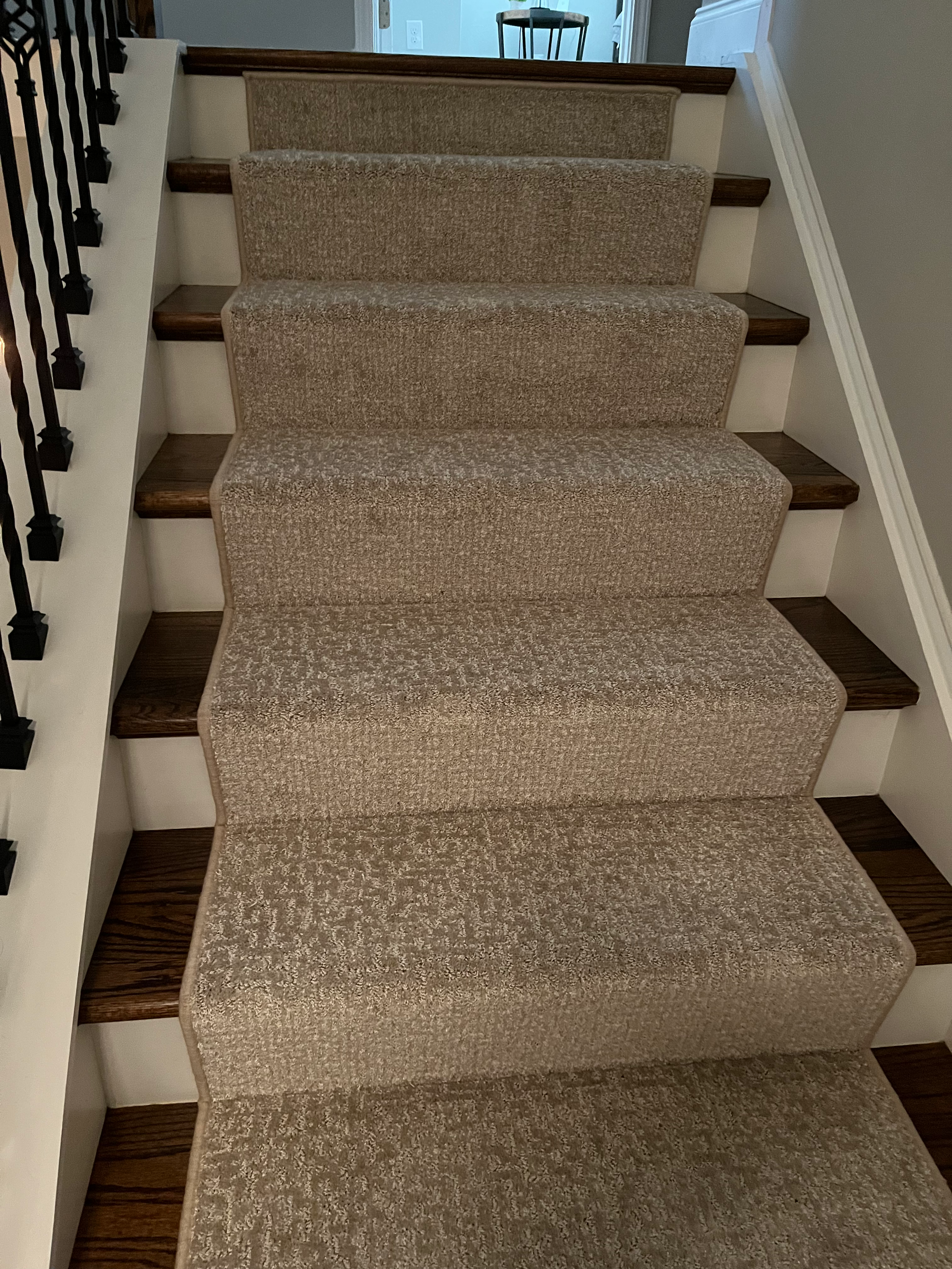 Staircase with carpeted steps and wooden treads; a white wall on the right, black railing on the left.