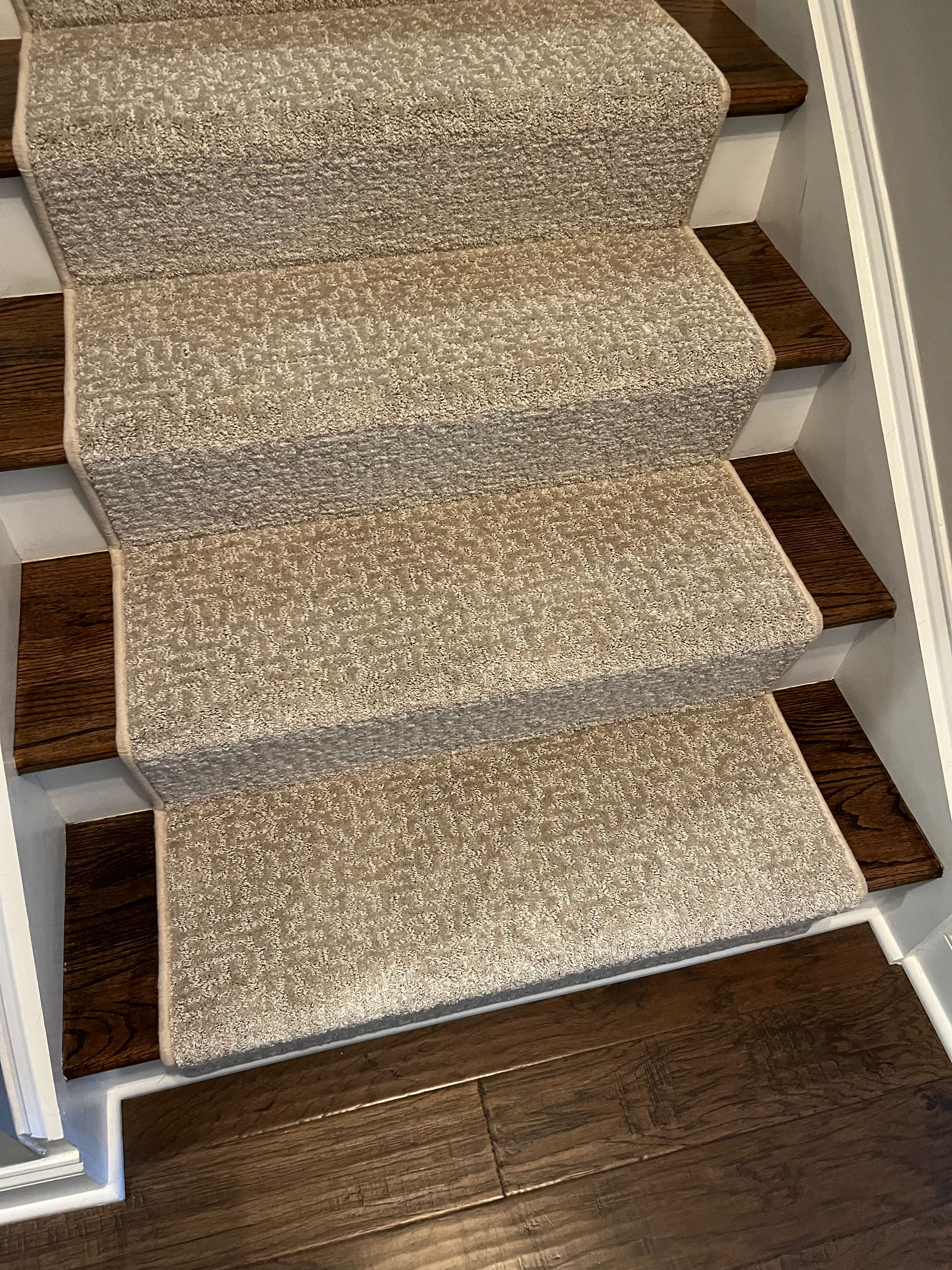Carpeted staircase with brown treads. The carpet is beige with flecks.