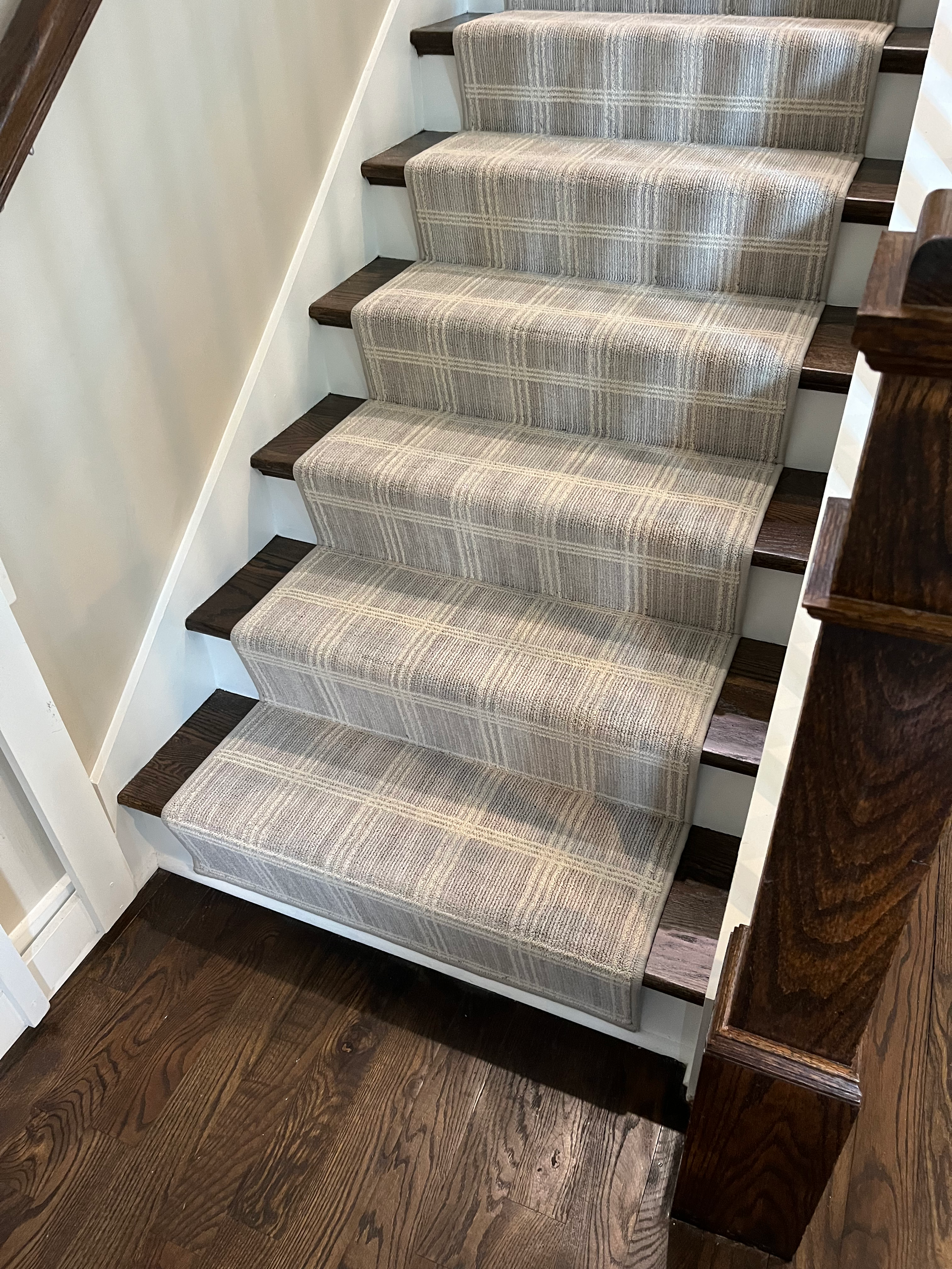 Staircase with grey patterned carpet runner, dark wood treads, and a white wall.