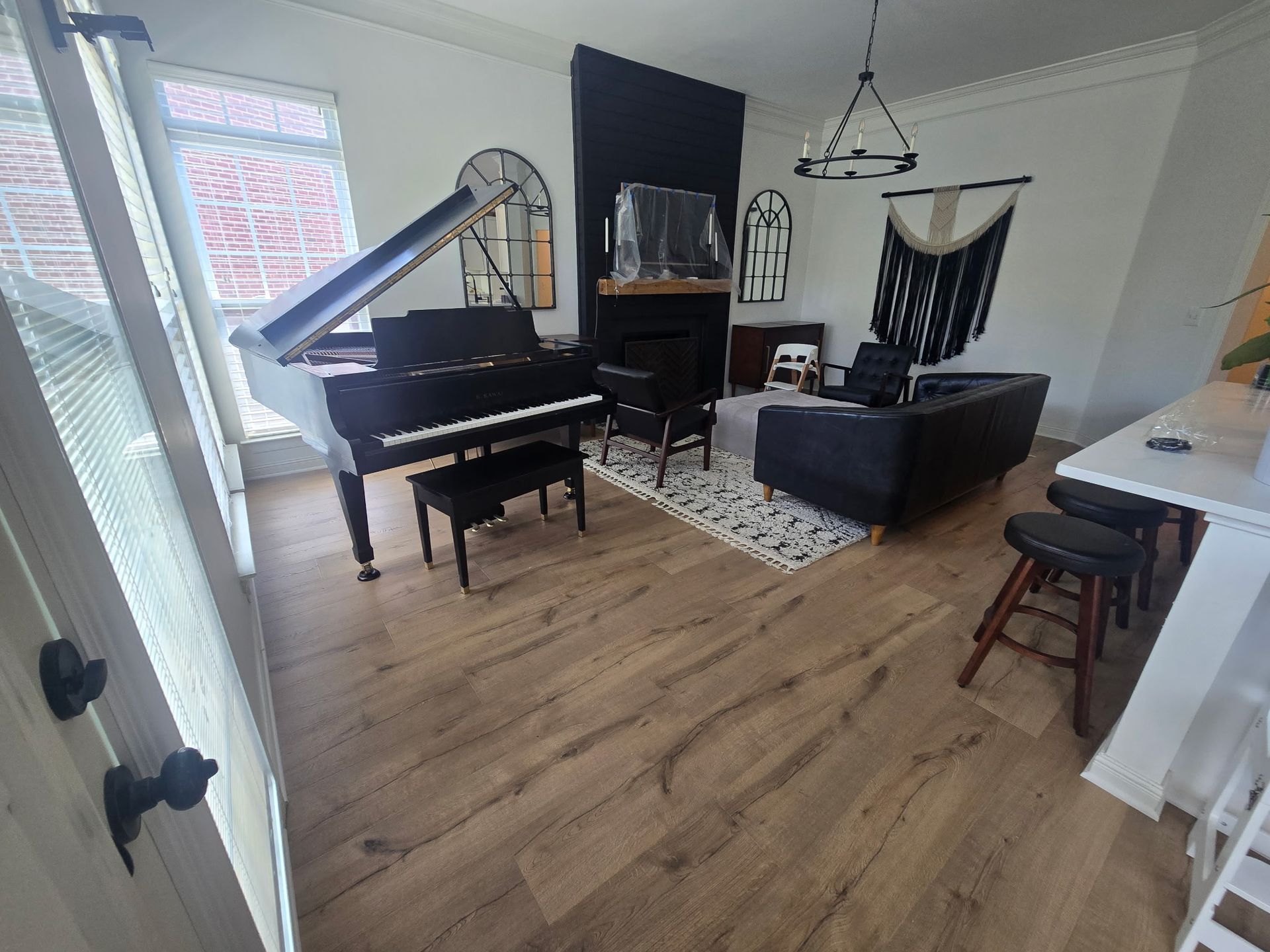 A room with a grand piano, black sofa, and rug. White walls and wood flooring.