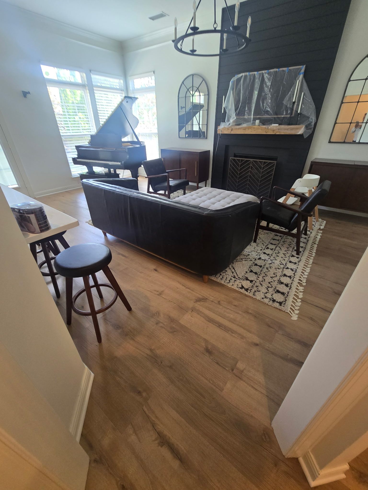 A modern living room with a grand piano, black sofa, fireplace, and wood flooring.