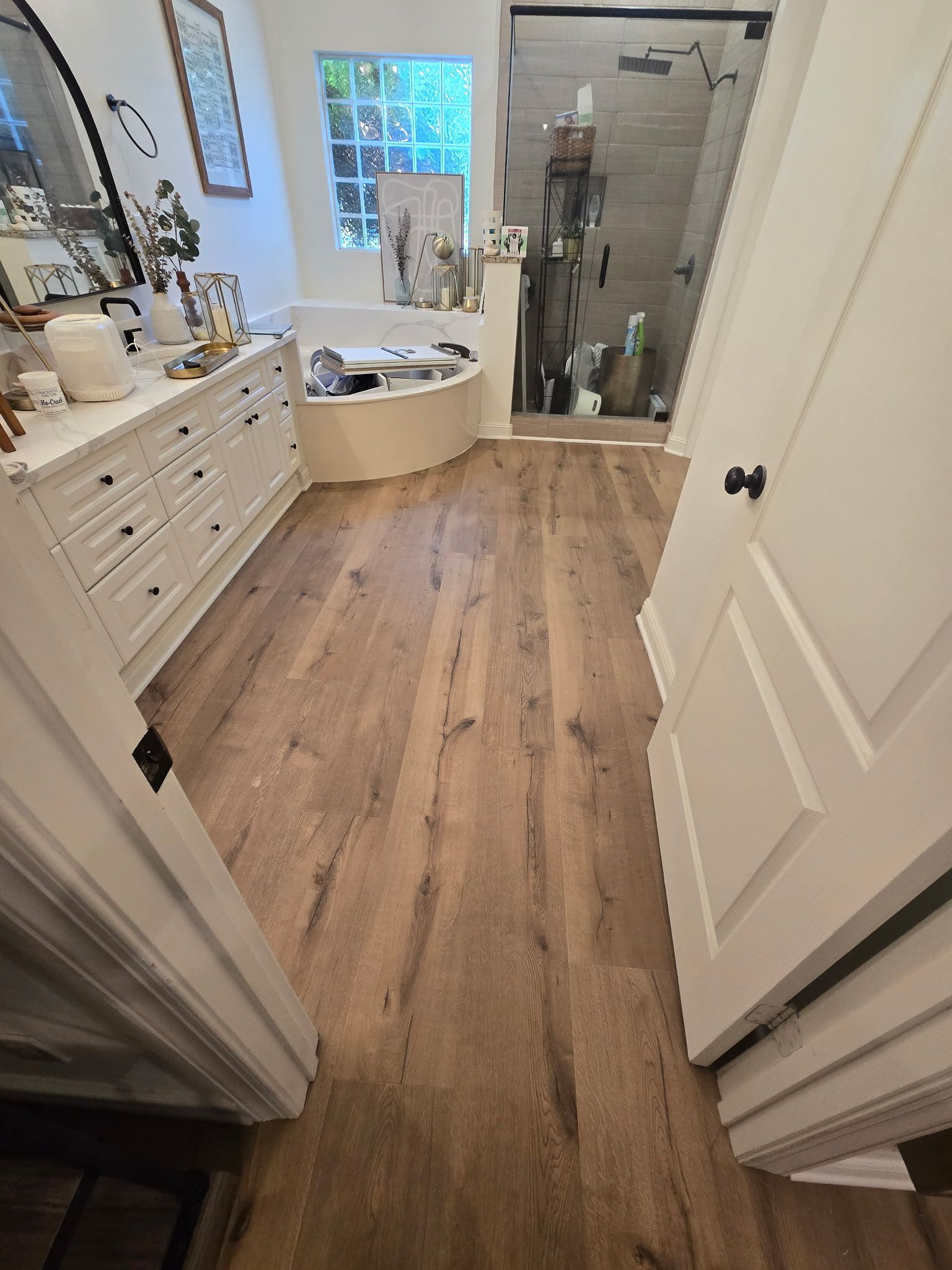 Bathroom with wood-look flooring, white vanity, and a glass shower.