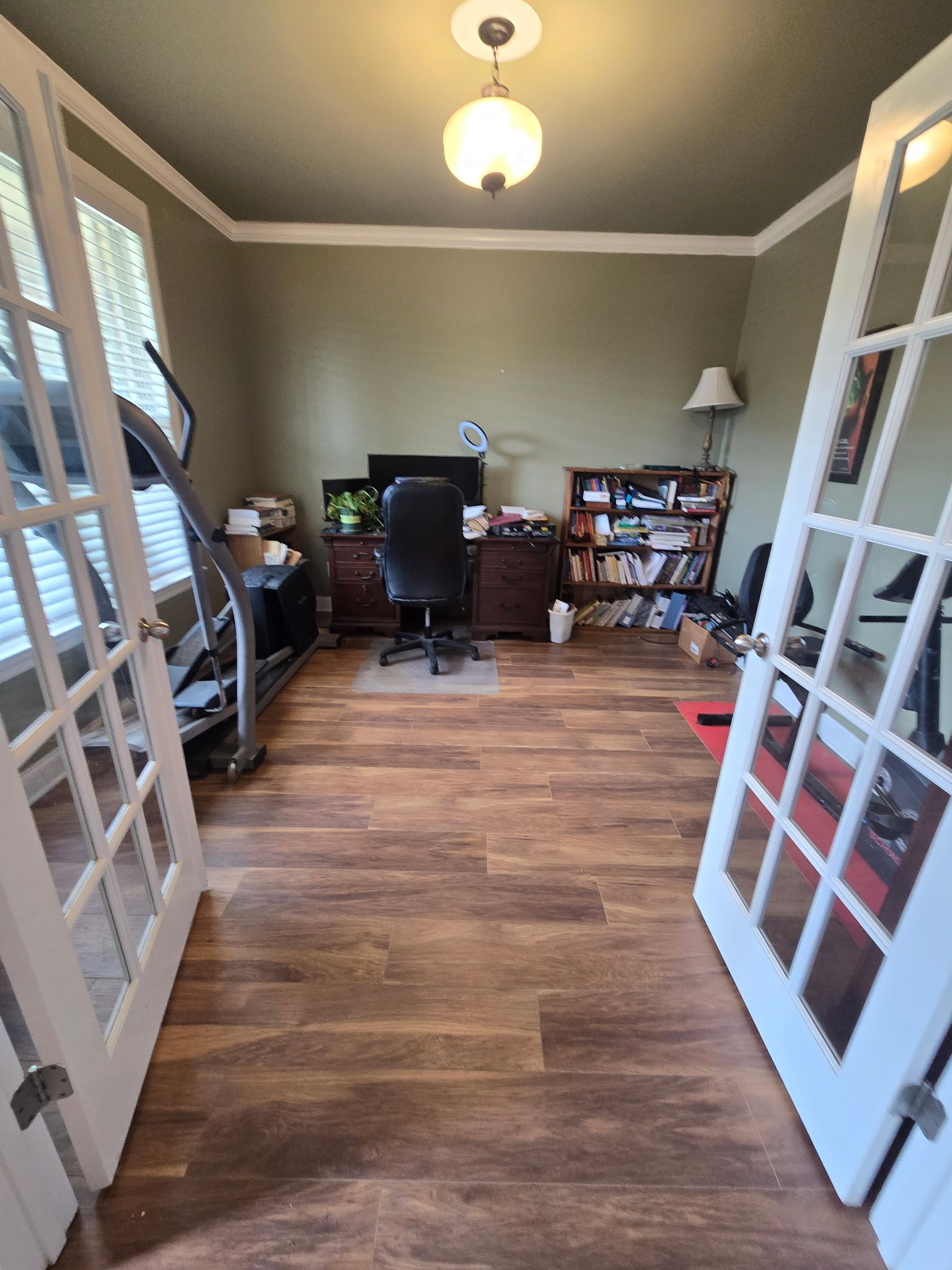 Office with hardwood floors, desk, treadmill, bookshelves, and French doors; olive walls and white trim.