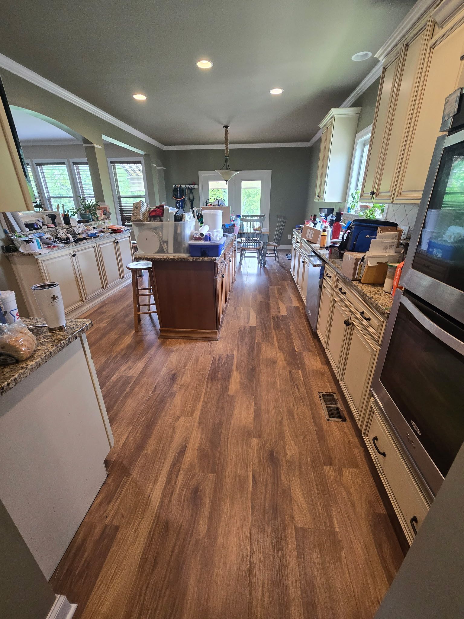 Kitchen with wood floors, cabinets, island, and appliances. Sunlight streams in, illuminating the space.
