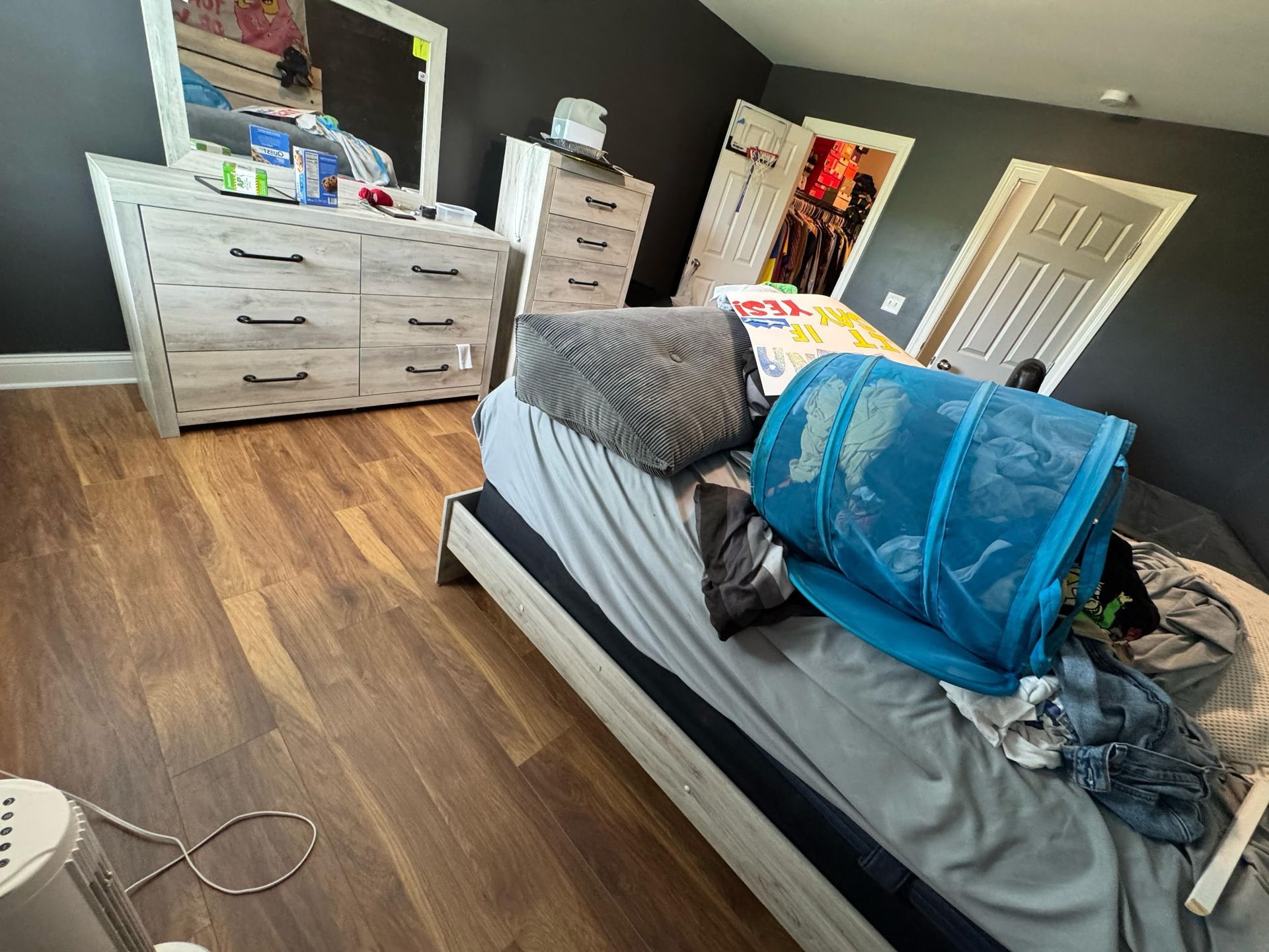 Bedroom with bed, dresser, open closet. Light wood floors, dark gray walls.