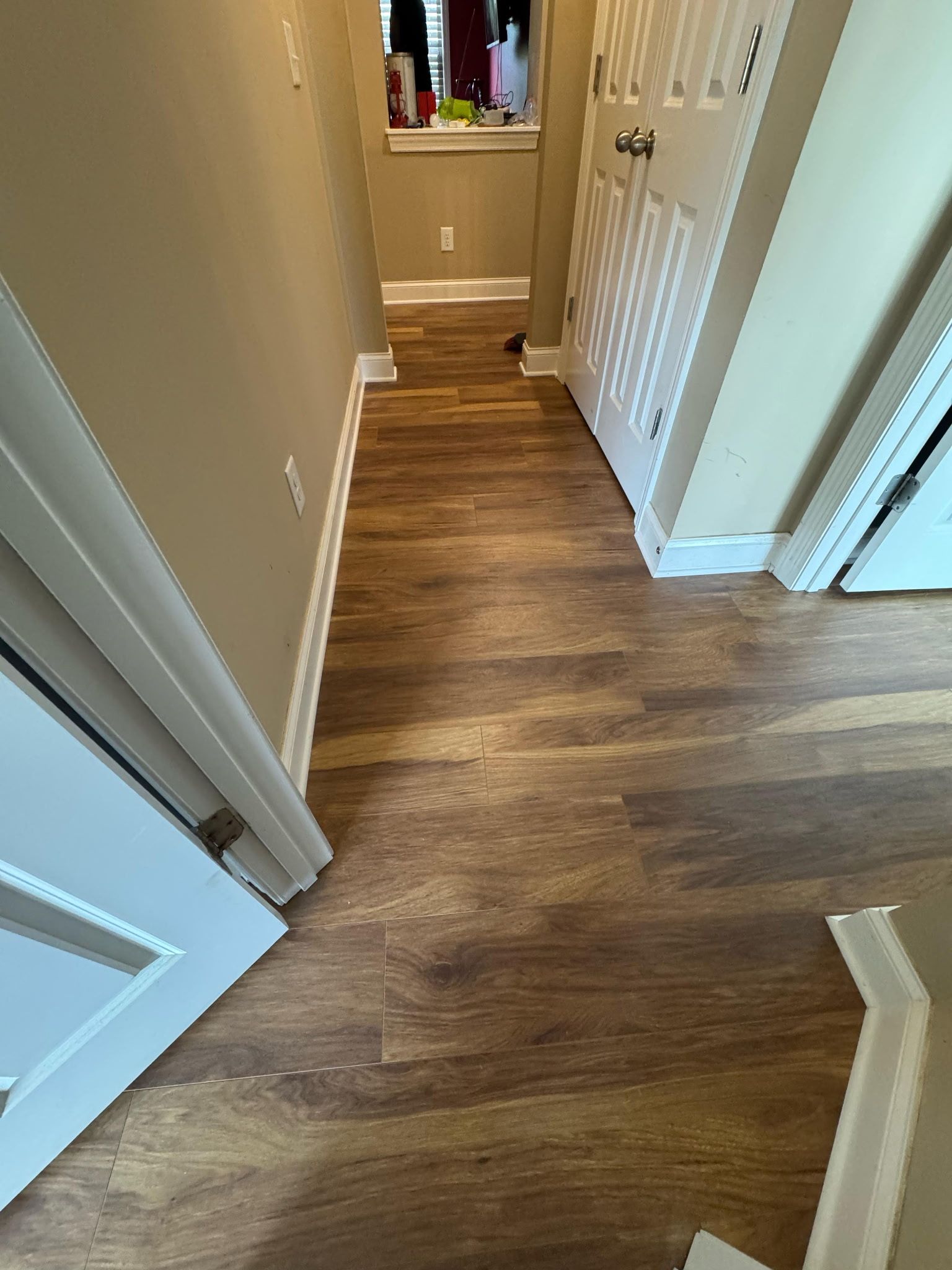 Narrow hallway with wood-look flooring, beige walls, white doors and trim.