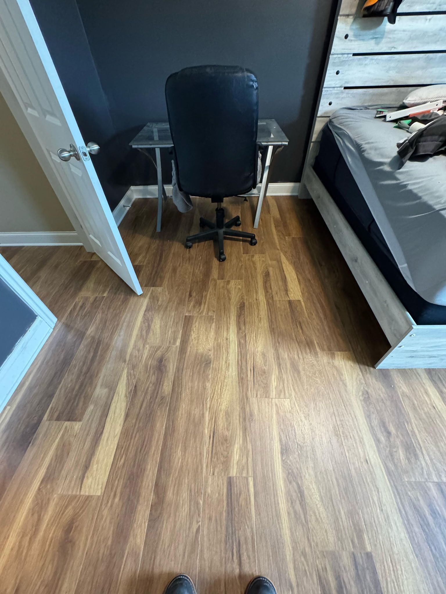 A bedroom with wood floors, desk and chair, a bed, and a doorway.