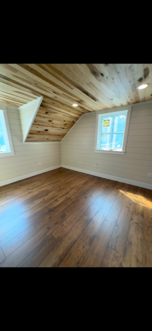 Empty room with wooden floor and ceiling, and white walls with two windows.