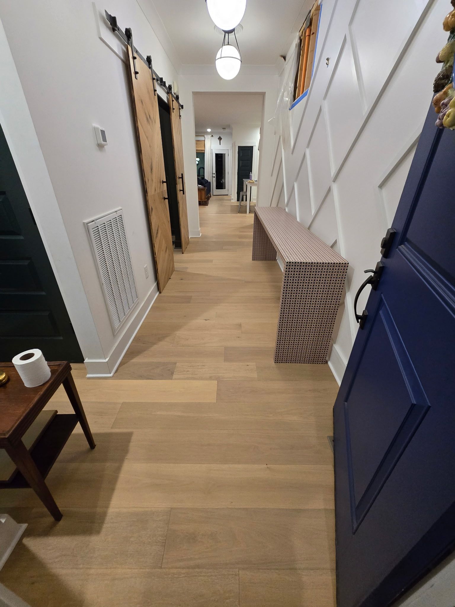 Hallway with light wood floor, blue door, wooden barn door, and white paneled wall.