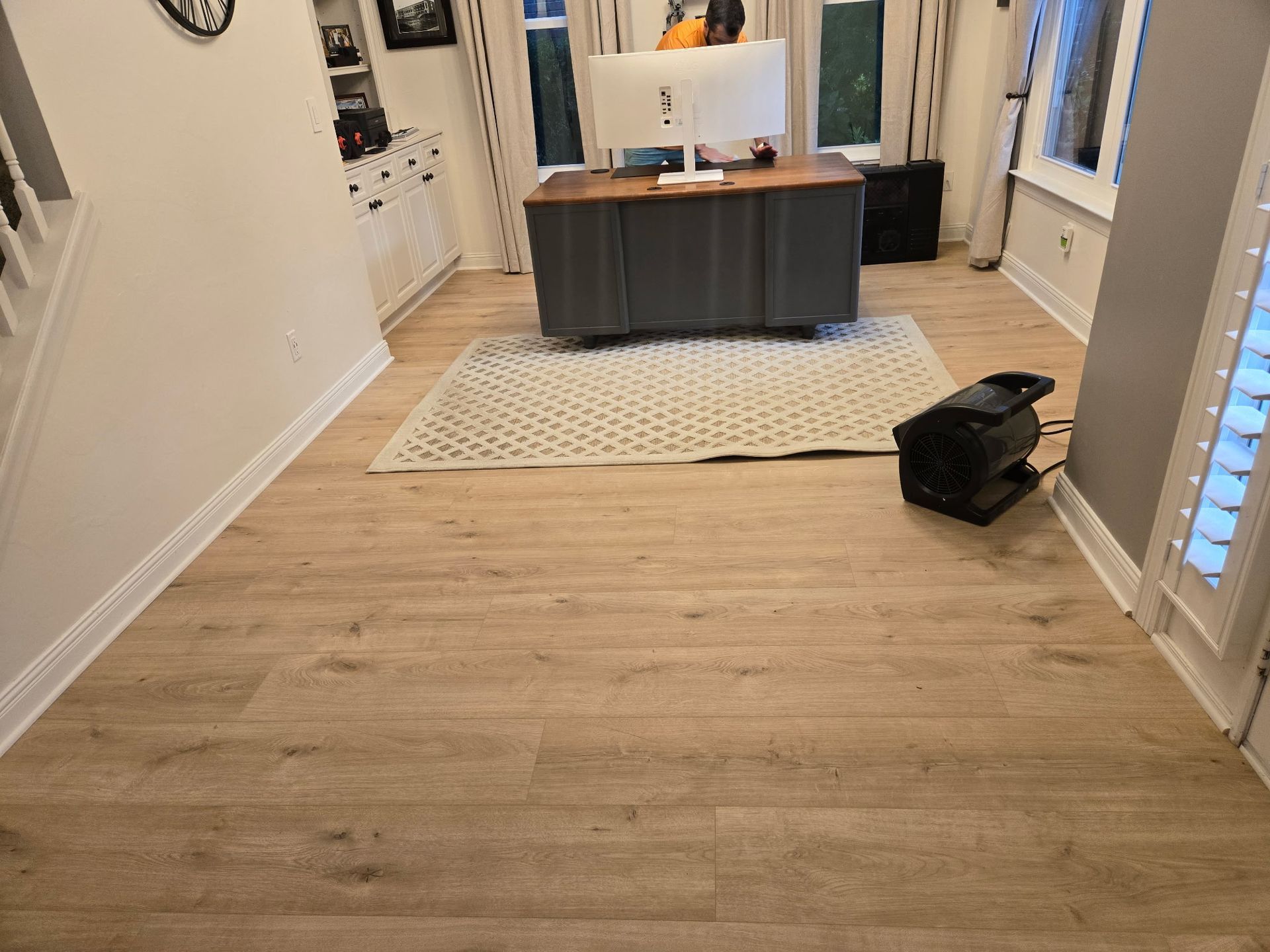 Light wood-look flooring in a home office. A desk with a computer sits on a rug. A space heater is visible.
