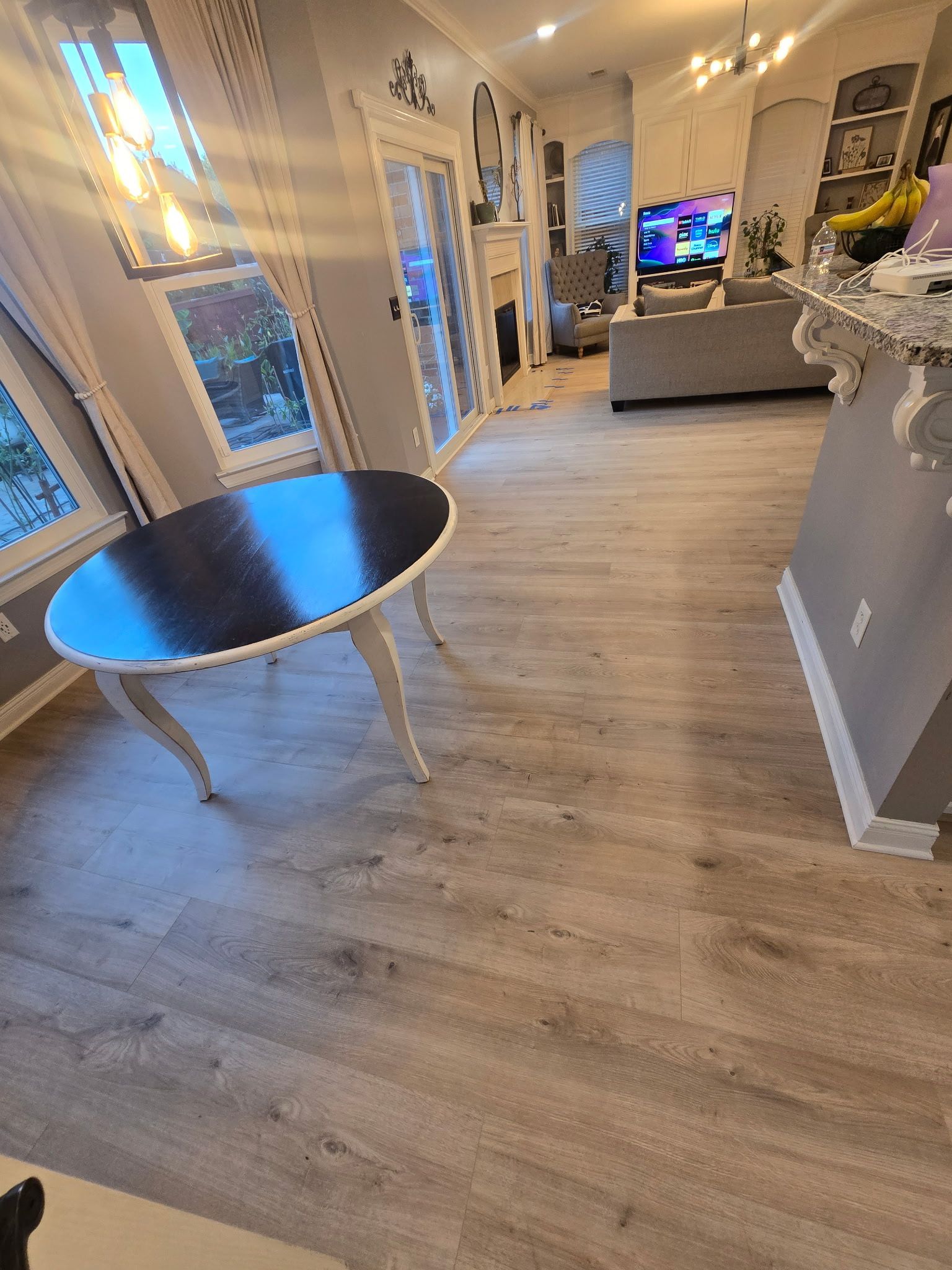 A room with a round dining table, light wood floors, and a view to a living area.