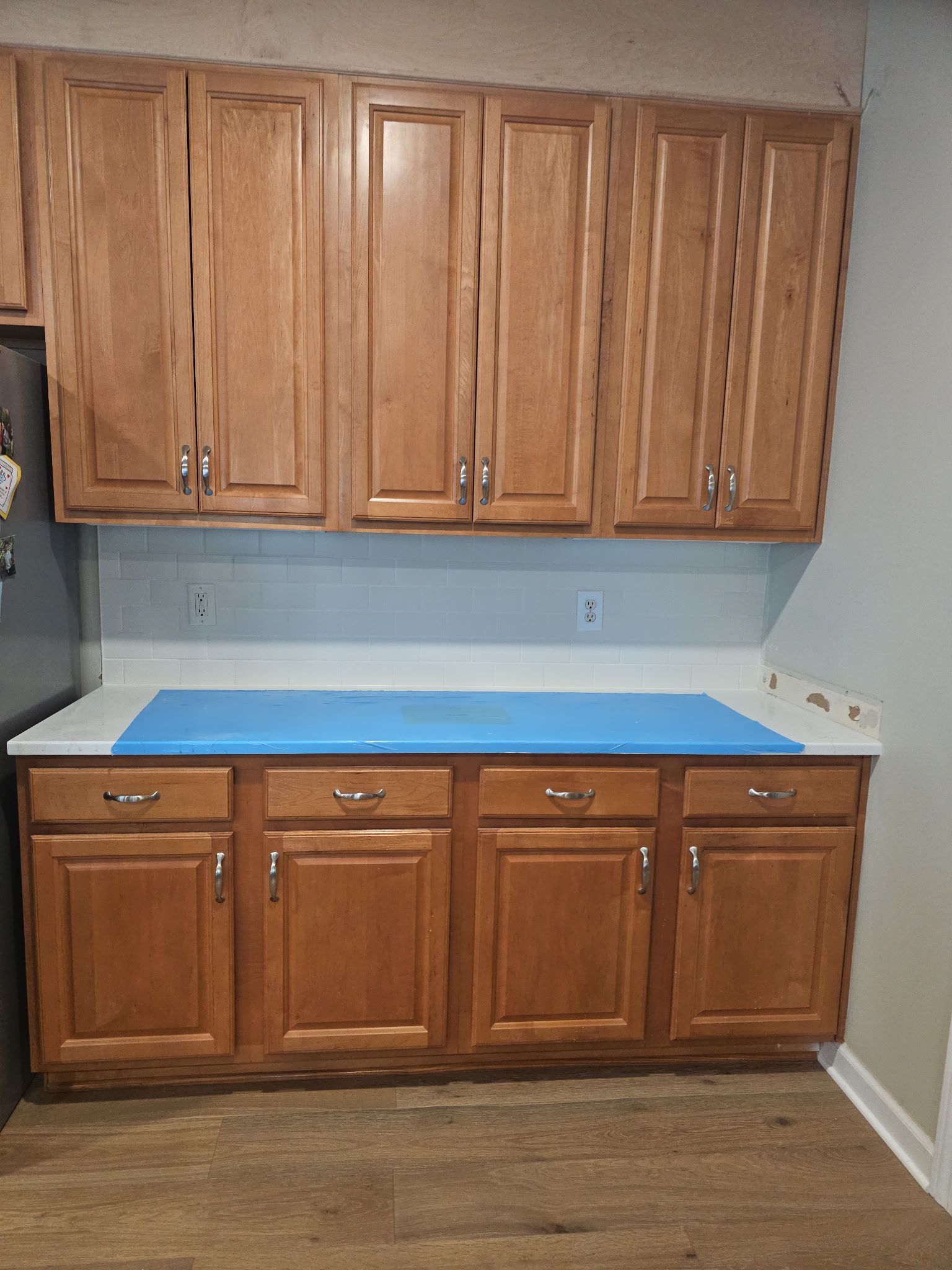 Kitchen cabinets: upper and lower wooden cabinets with light countertops and a blue covering.