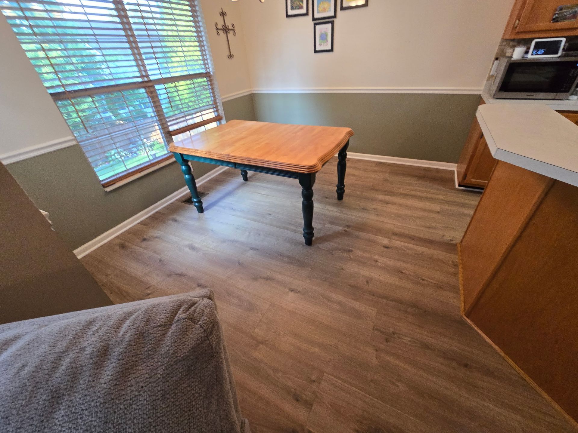 Dining room with wooden table, green legs, and wood-look flooring. Light coming through window.