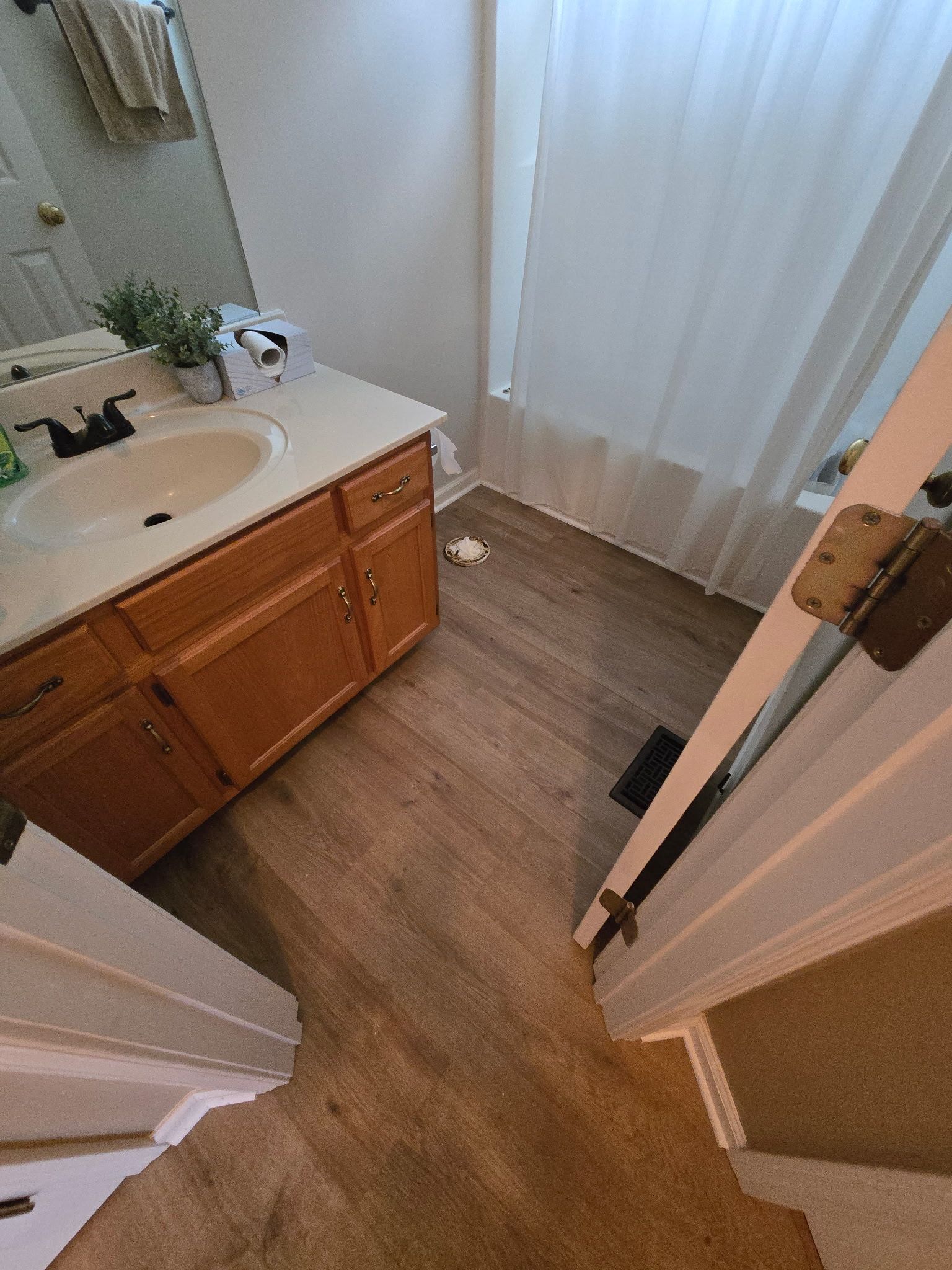 Bathroom with wood-look floor, wood vanity, sink, white shower curtain, and open door.