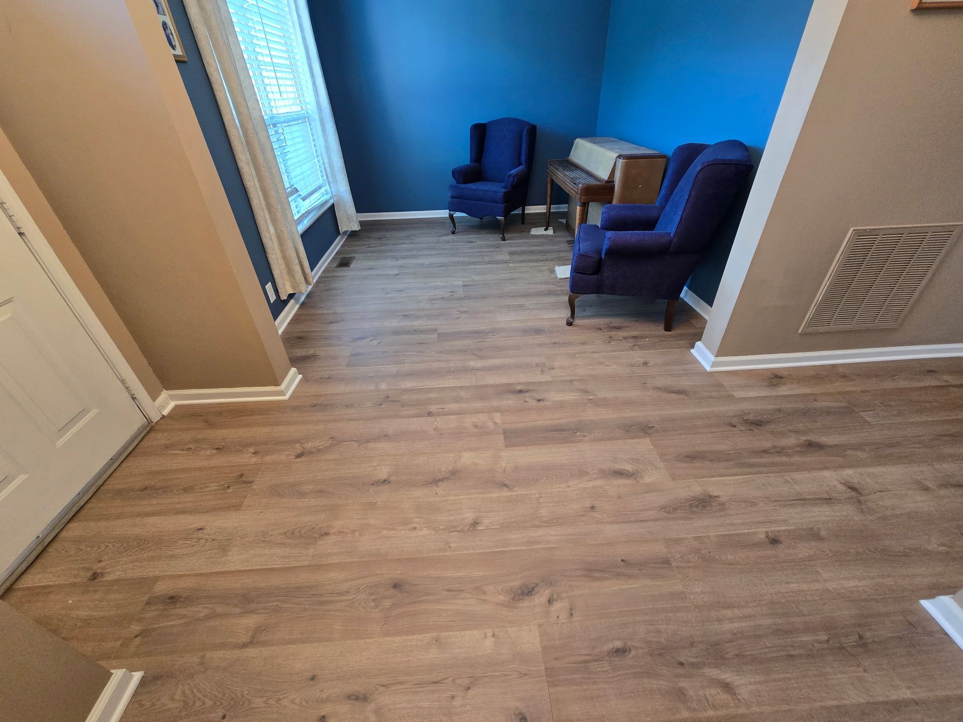 Room with wood-look flooring, blue walls, two blue chairs, and a piano.