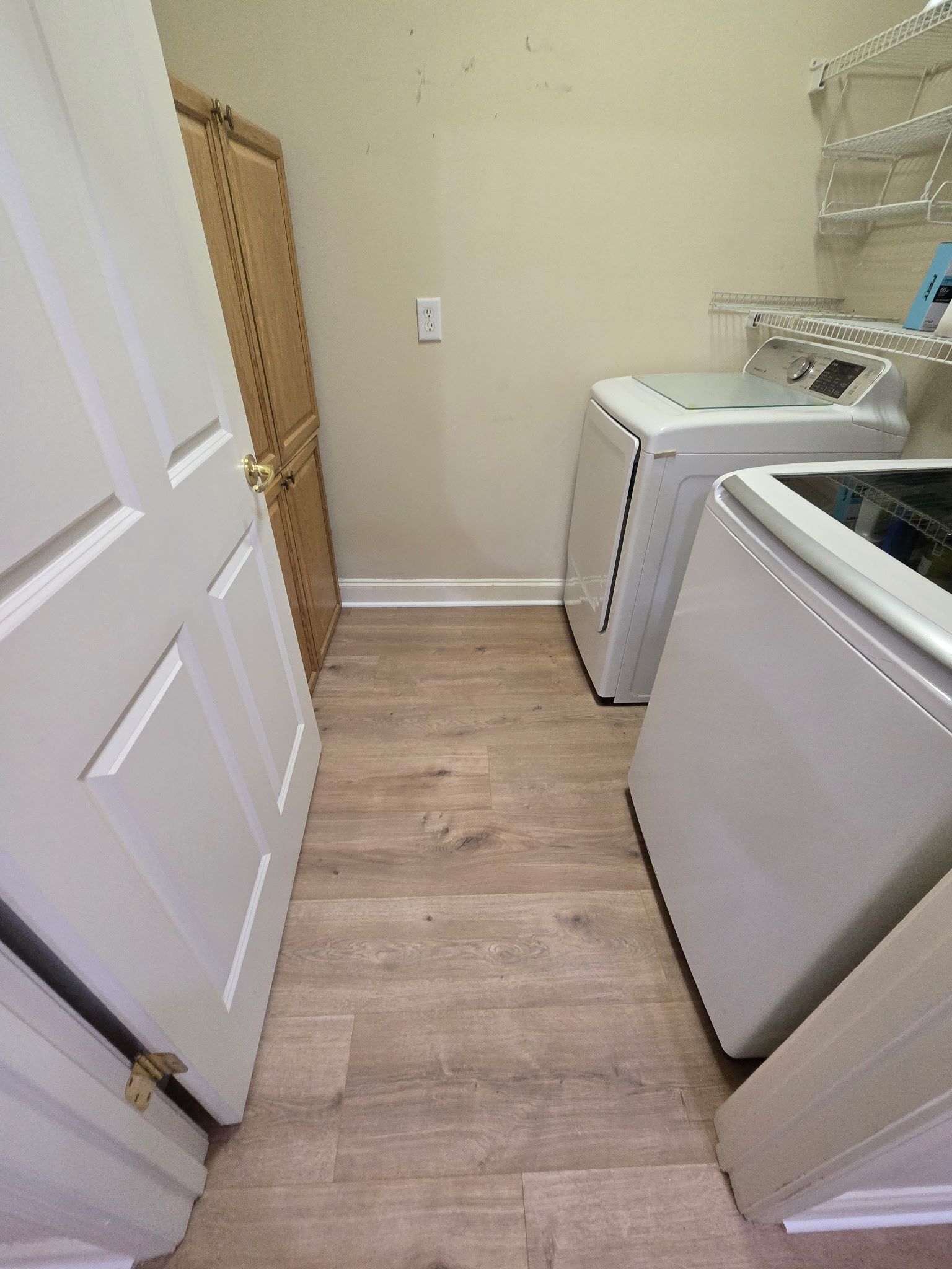 Laundry room with a washing machine, dryer, storage cabinet, and wooden-look flooring.