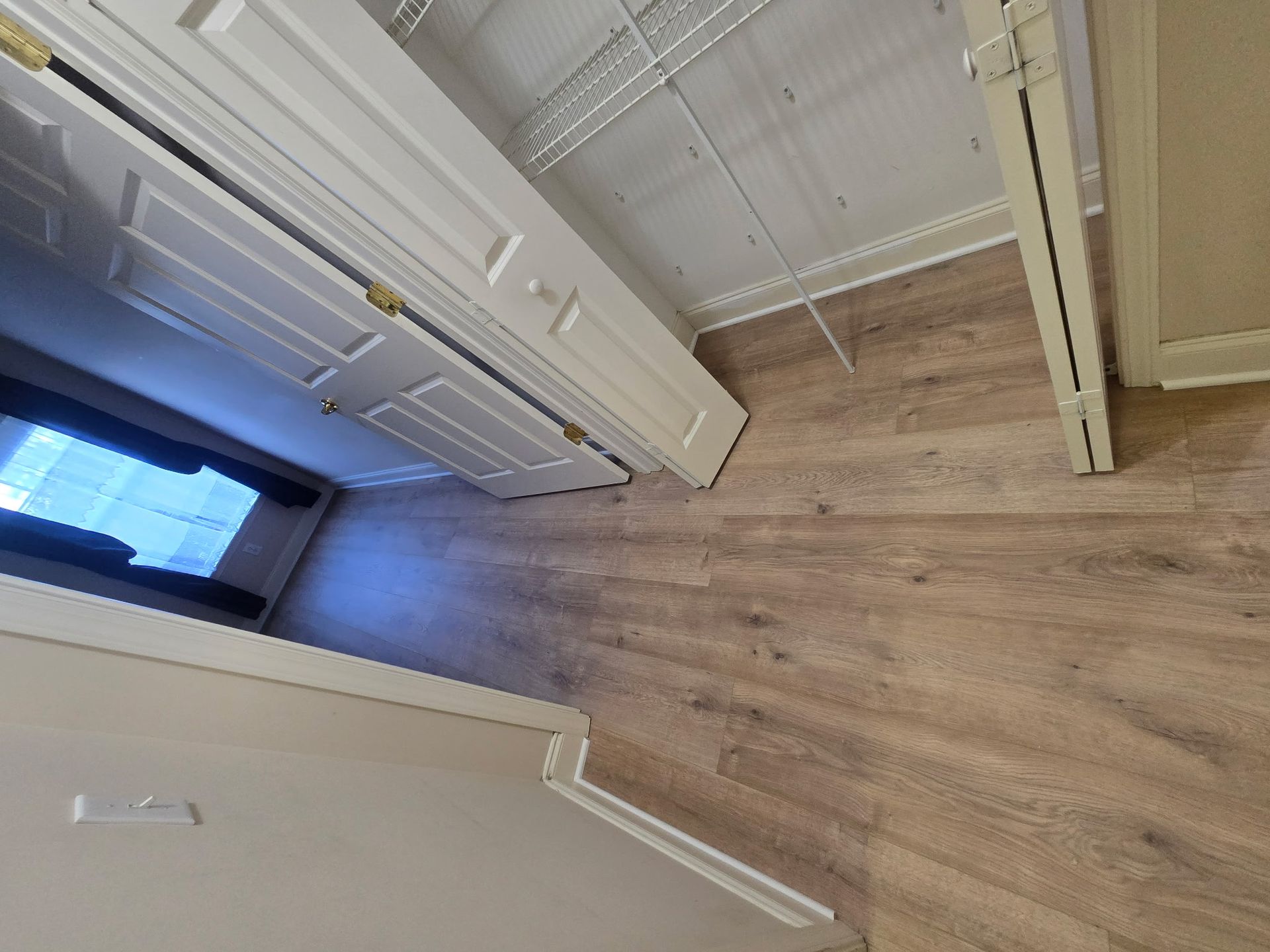 A room with light wood floors, a closet, and a window.