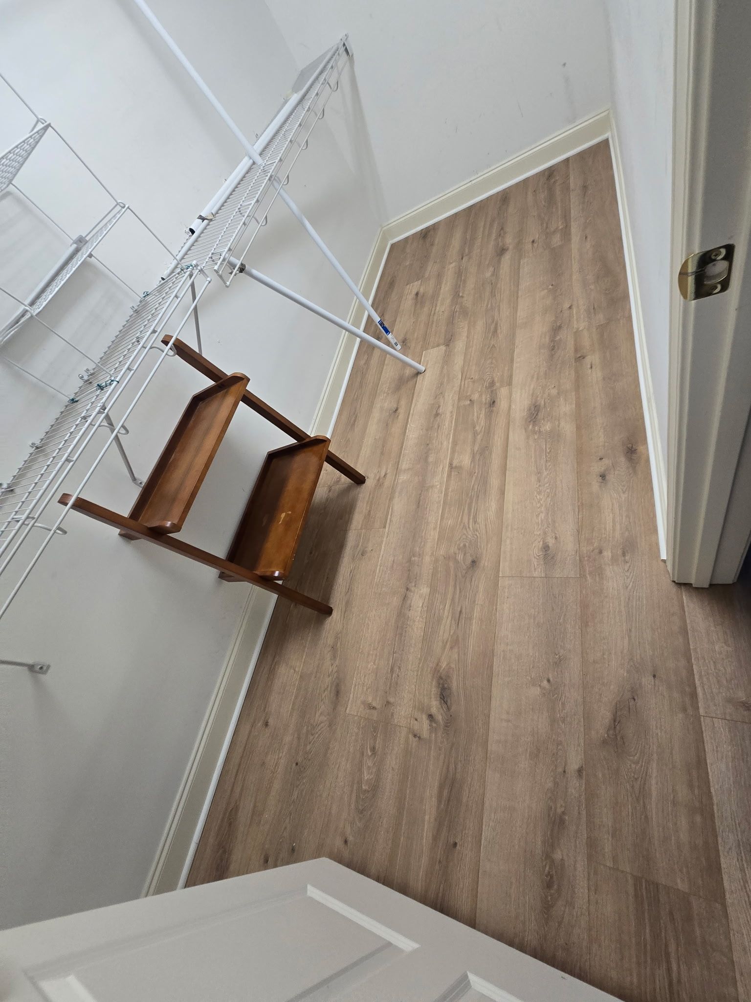 Closet interior with wire shelving, brown floor, wooden shelf, and door.