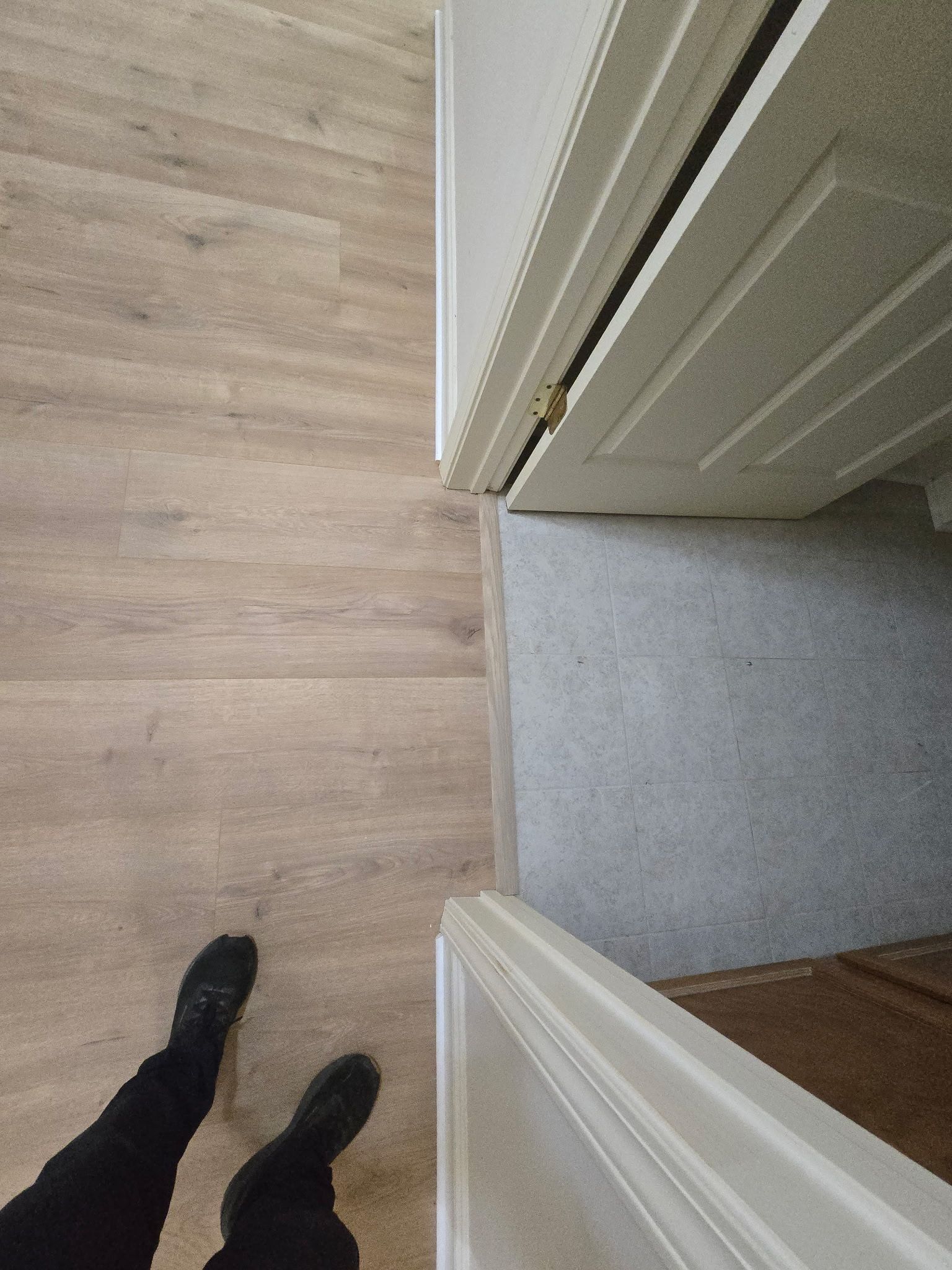 Person standing in doorway, light wood floor meets gray carpet. Door frames are white.