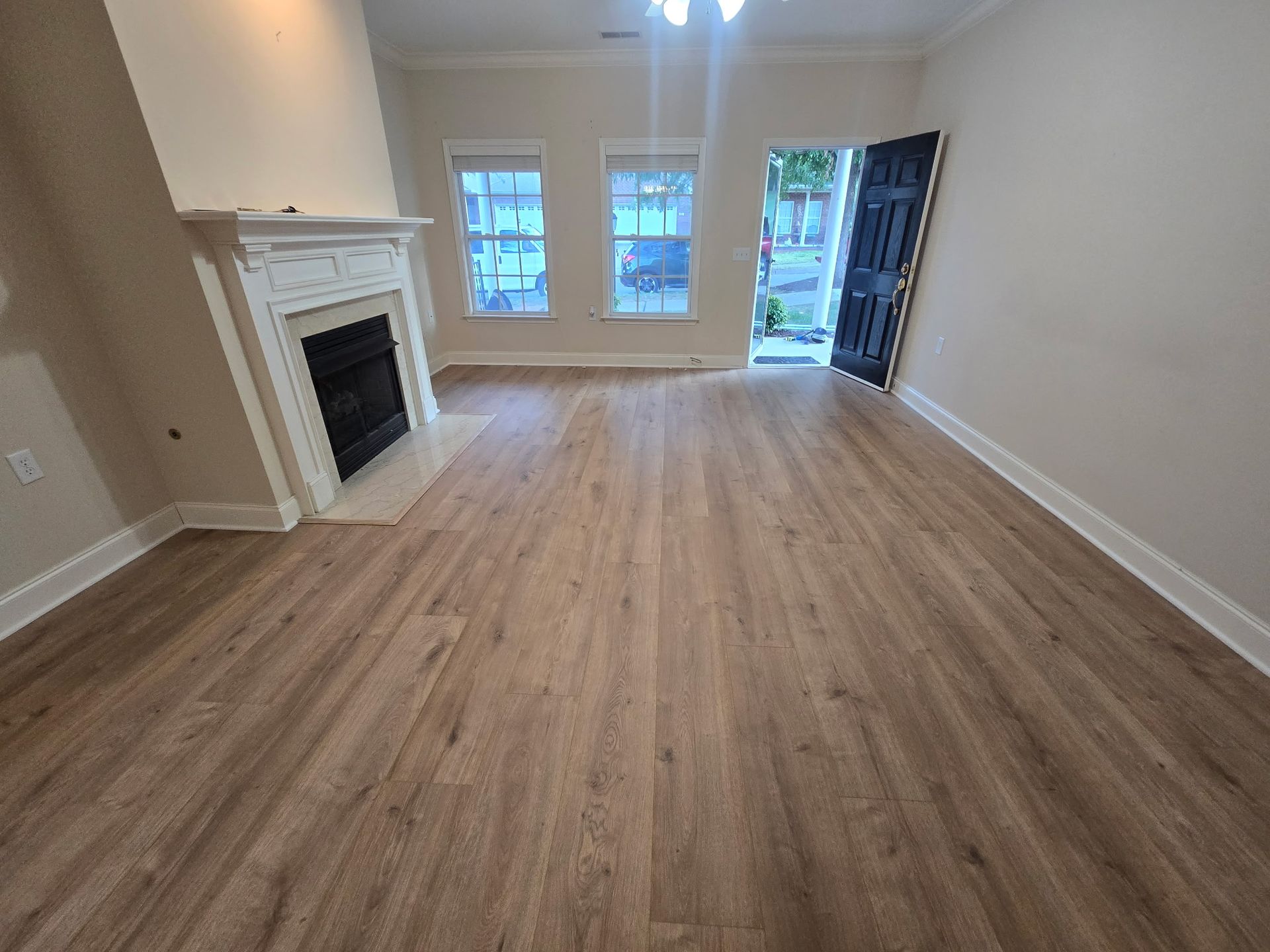 Living room with fireplace, three windows, open door, and wood-look flooring.