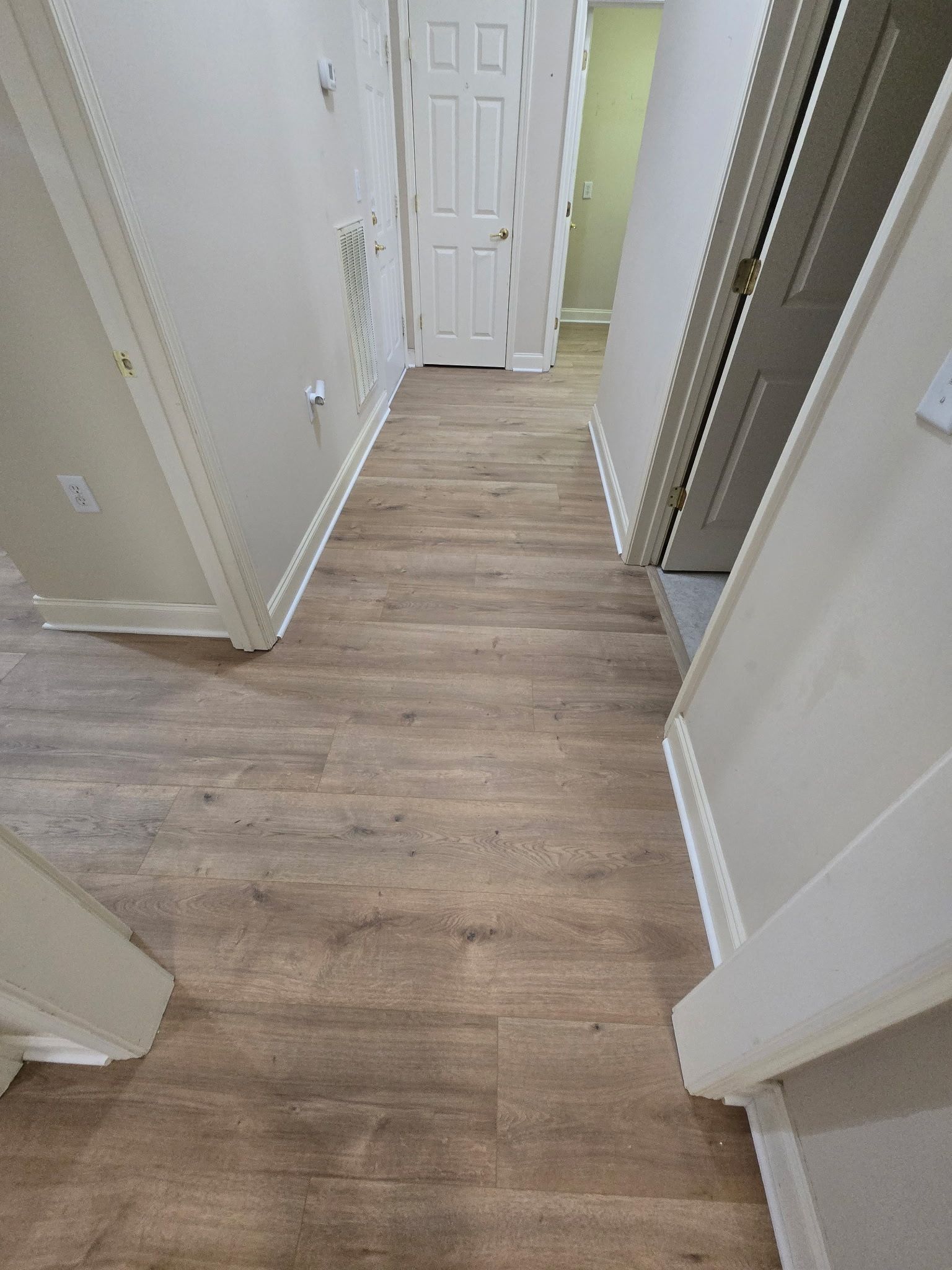 Narrow hallway with wood-look flooring, white walls, doors, and trim.
