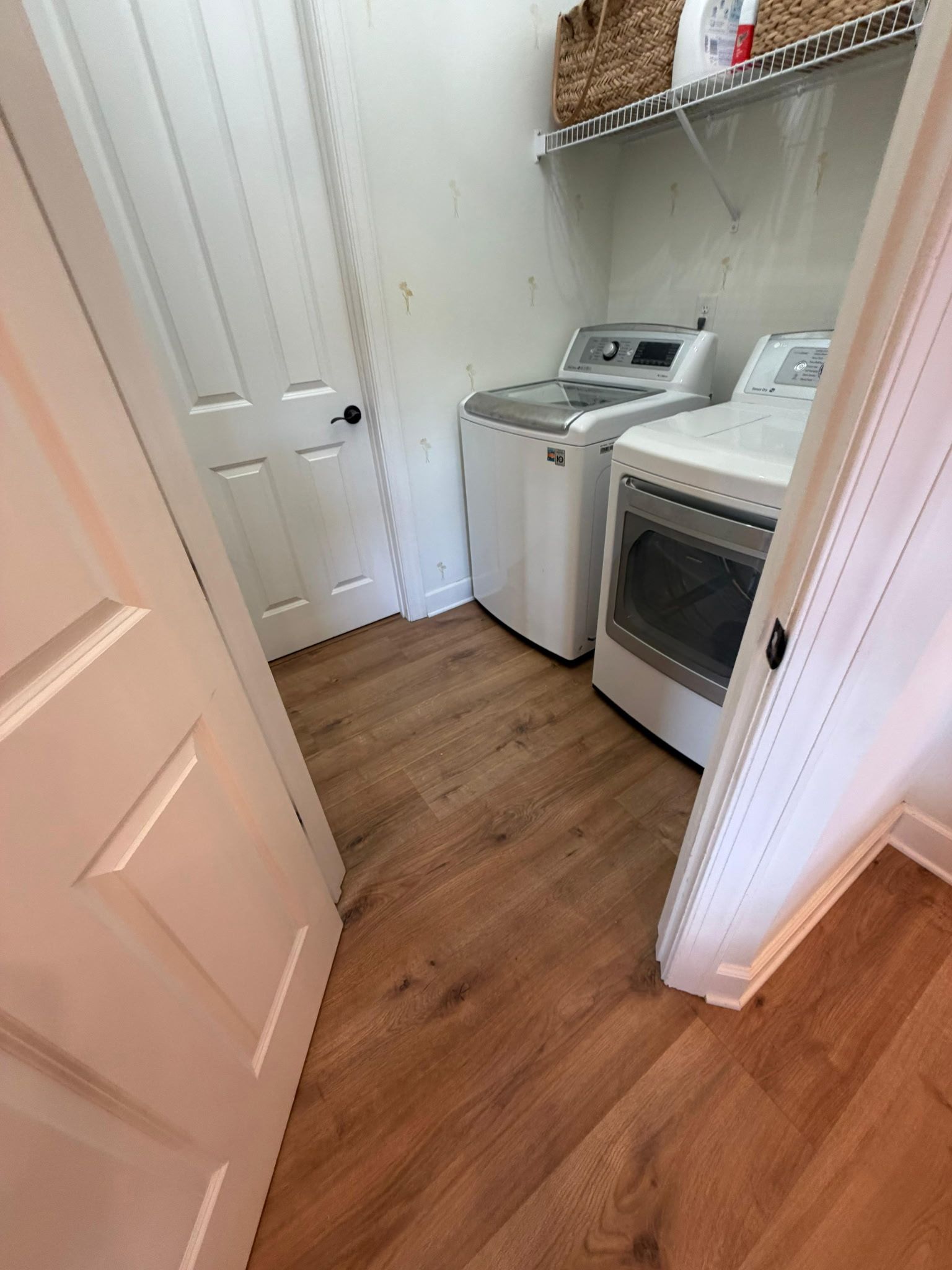 Laundry room with white appliances, wooden floor, and a door.