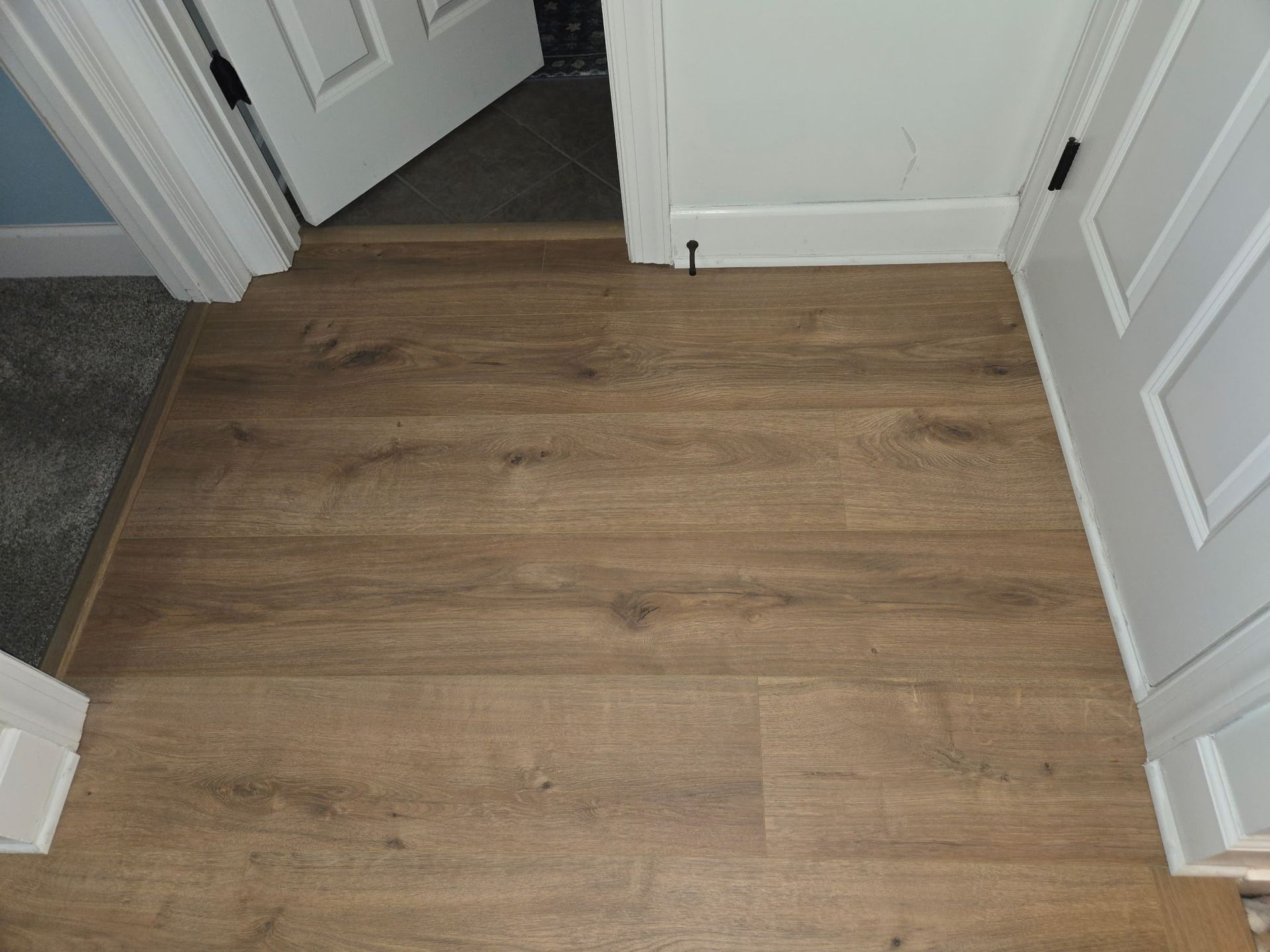 Brown wood-look flooring installed in a doorway. A partially open white door is visible.