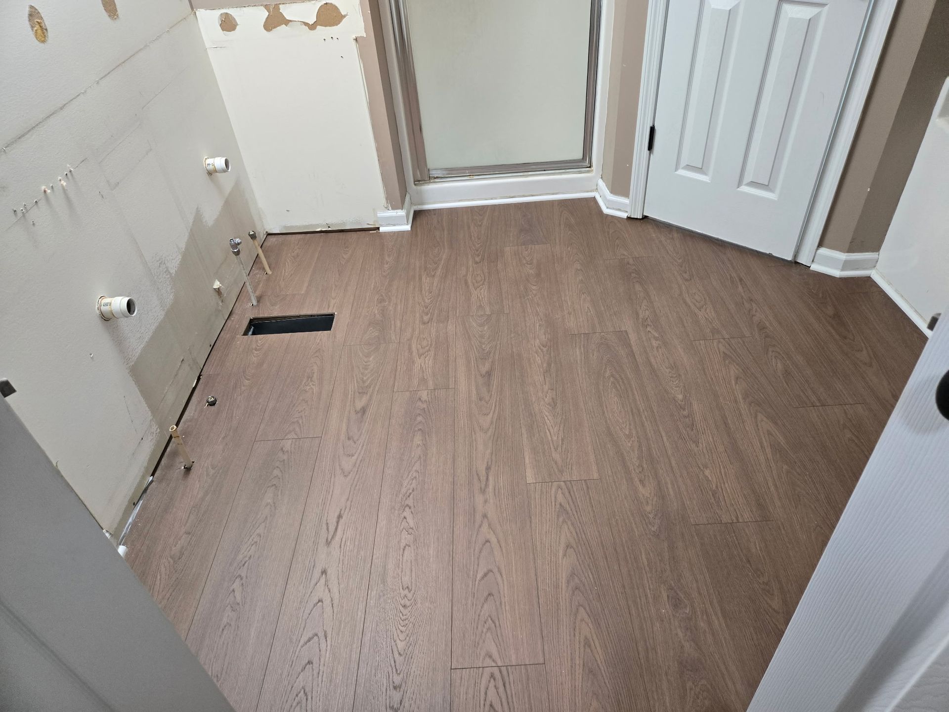 Empty beige hallway with wood flooring, white doors, and a floor vent near a closet cabinet.