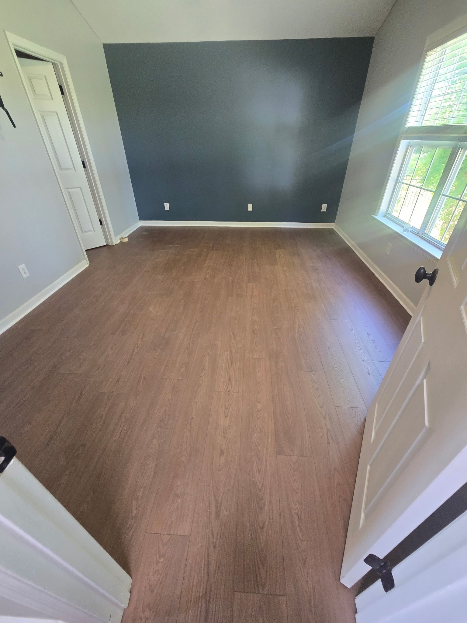 Empty room with gray walls, wood flooring, and a large window letting in daylight.