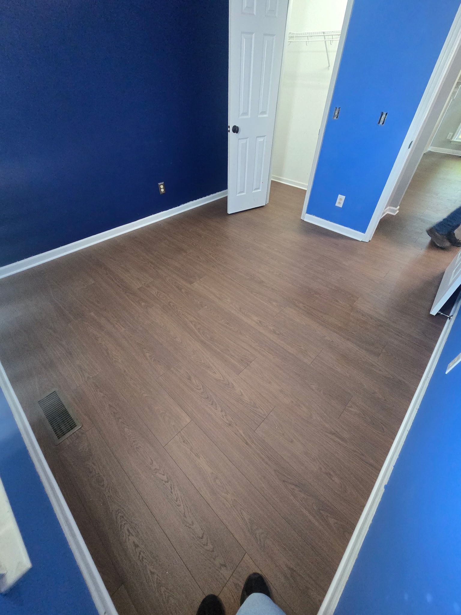 Empty room with blue walls, brown wood floor, and an open white door.