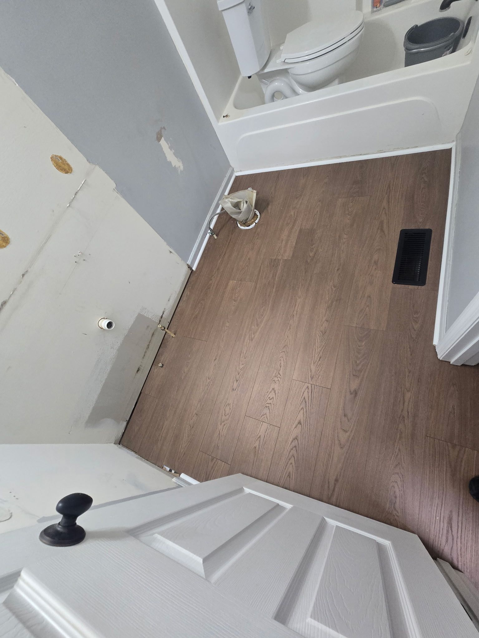 Small bathroom with tan floor, white fixtures, open door, and sink visible in the corner.