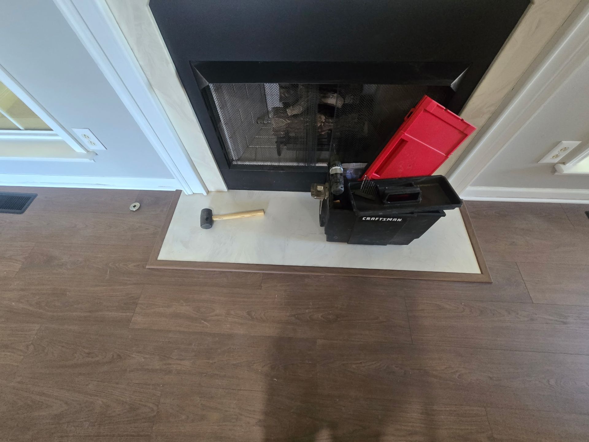 Black fireplace opening with a red toolbox and black bag on a white mat in front of it