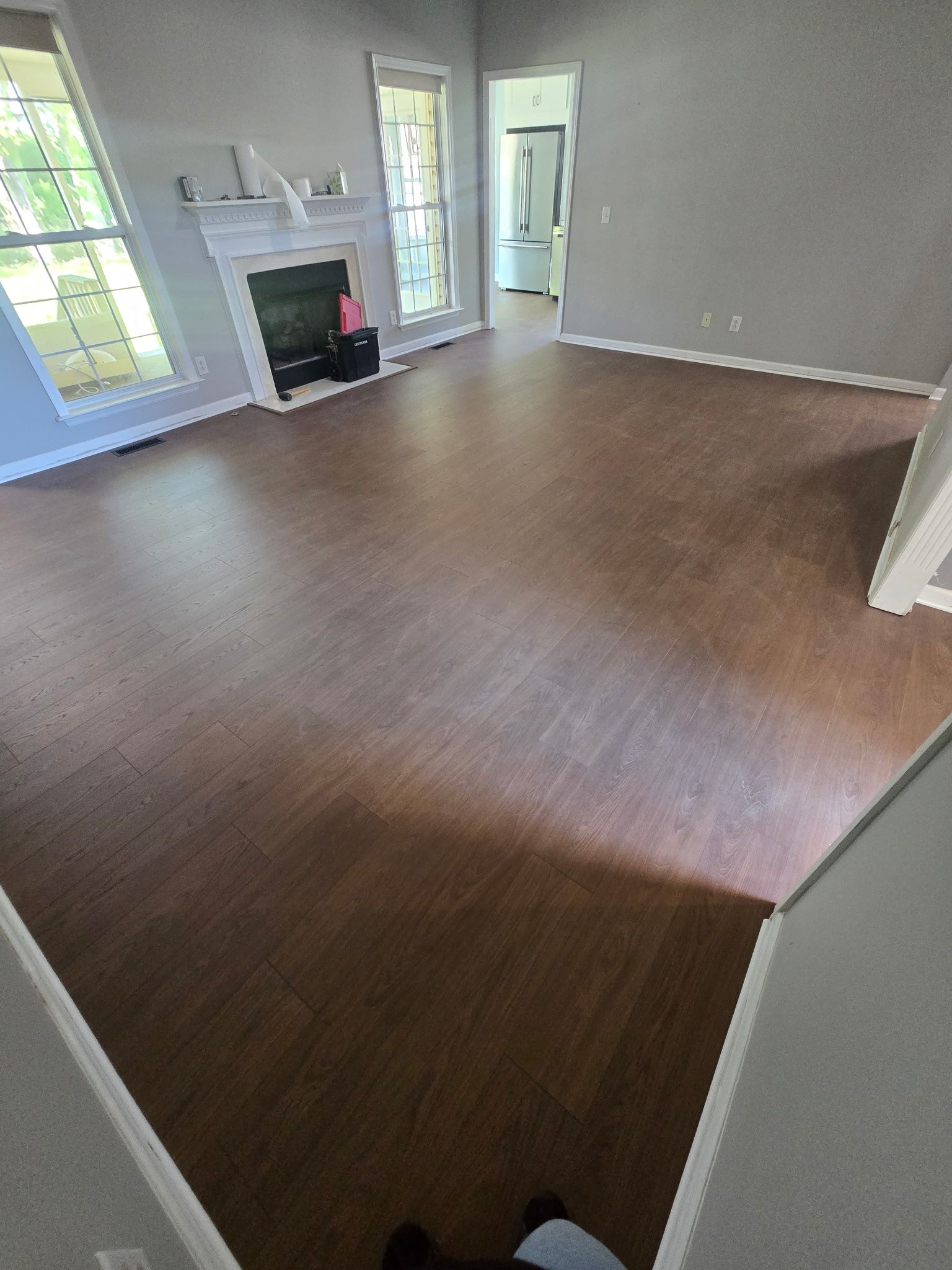 Empty living room with brown wood-look floor, white walls, fireplace, and French doors.